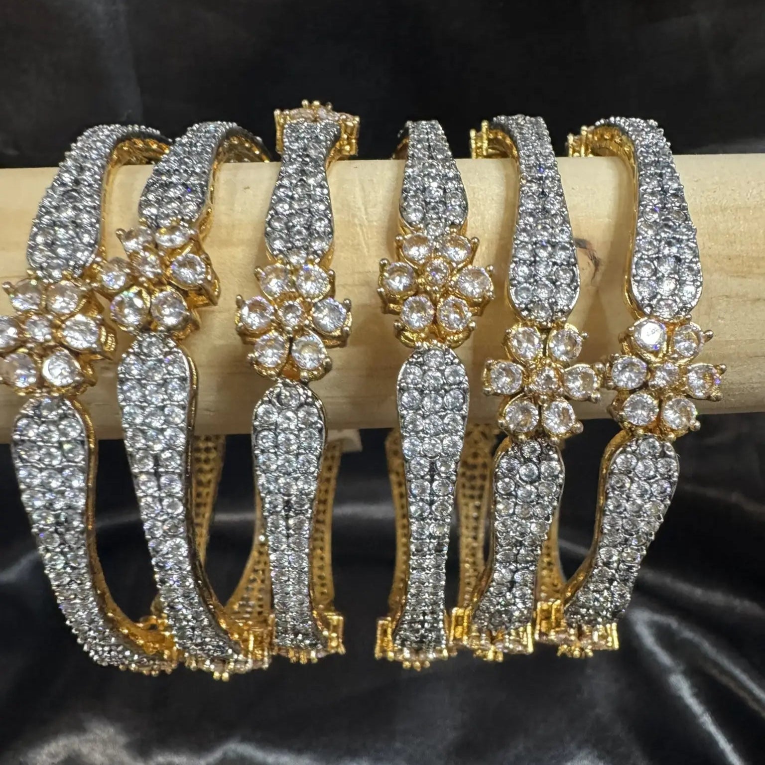 Gold-plated, American diamond bangles with flower patterns and clear gemstones on a wooden stick and silk cloth on the background