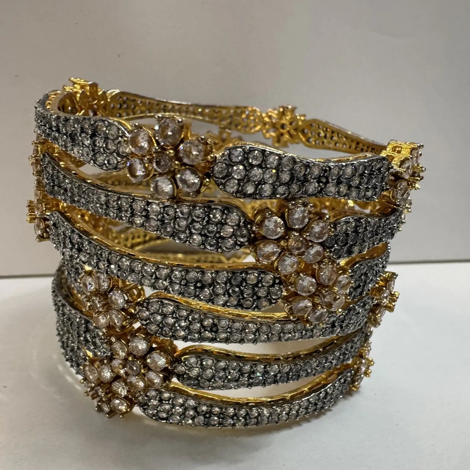 Gold-plated, American diamond bangles with flower patterns and clear gemstones on a white background