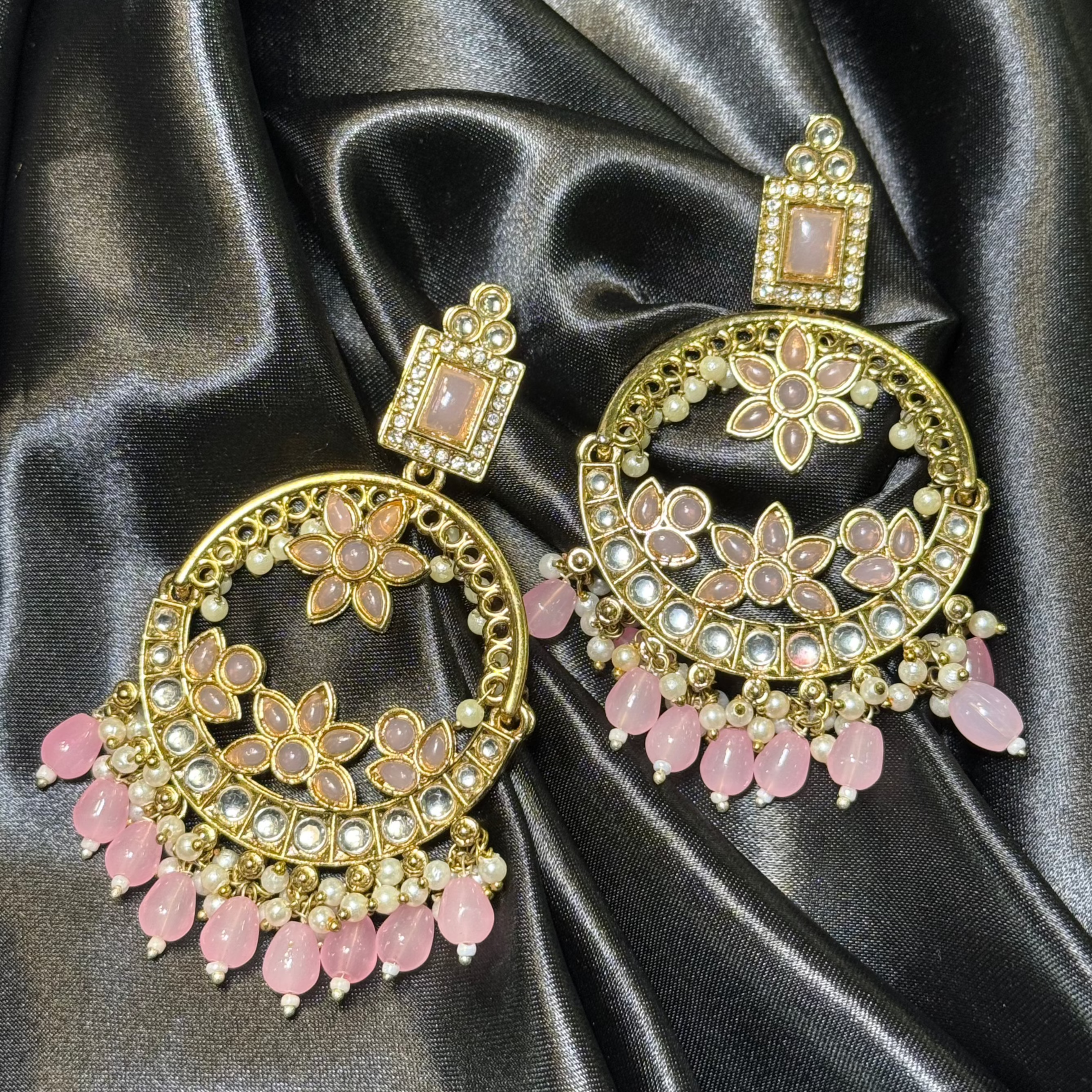 Ornate gold and pink earrings on black satin fabric