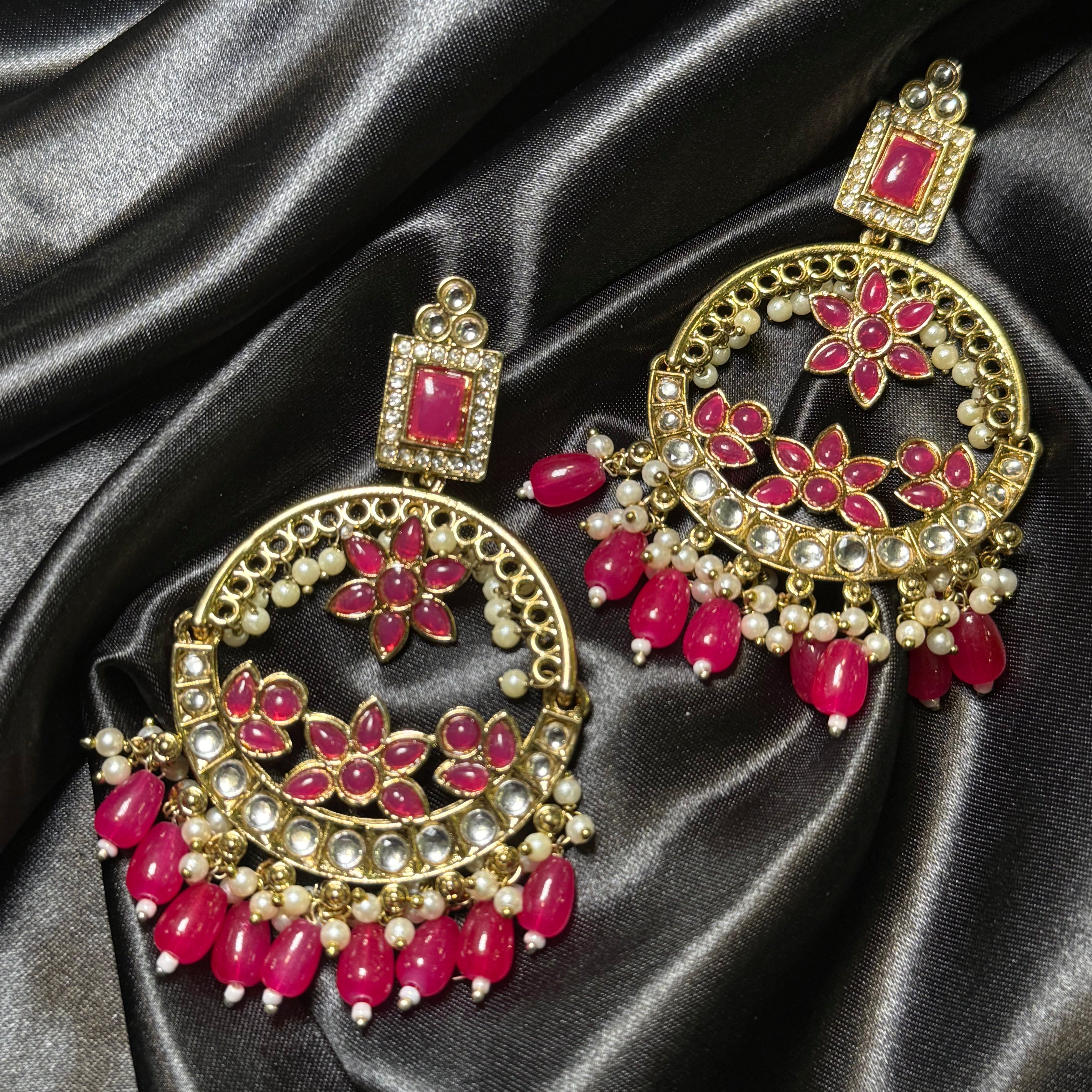 Ornate earrings with pink gemstones on a black satin background