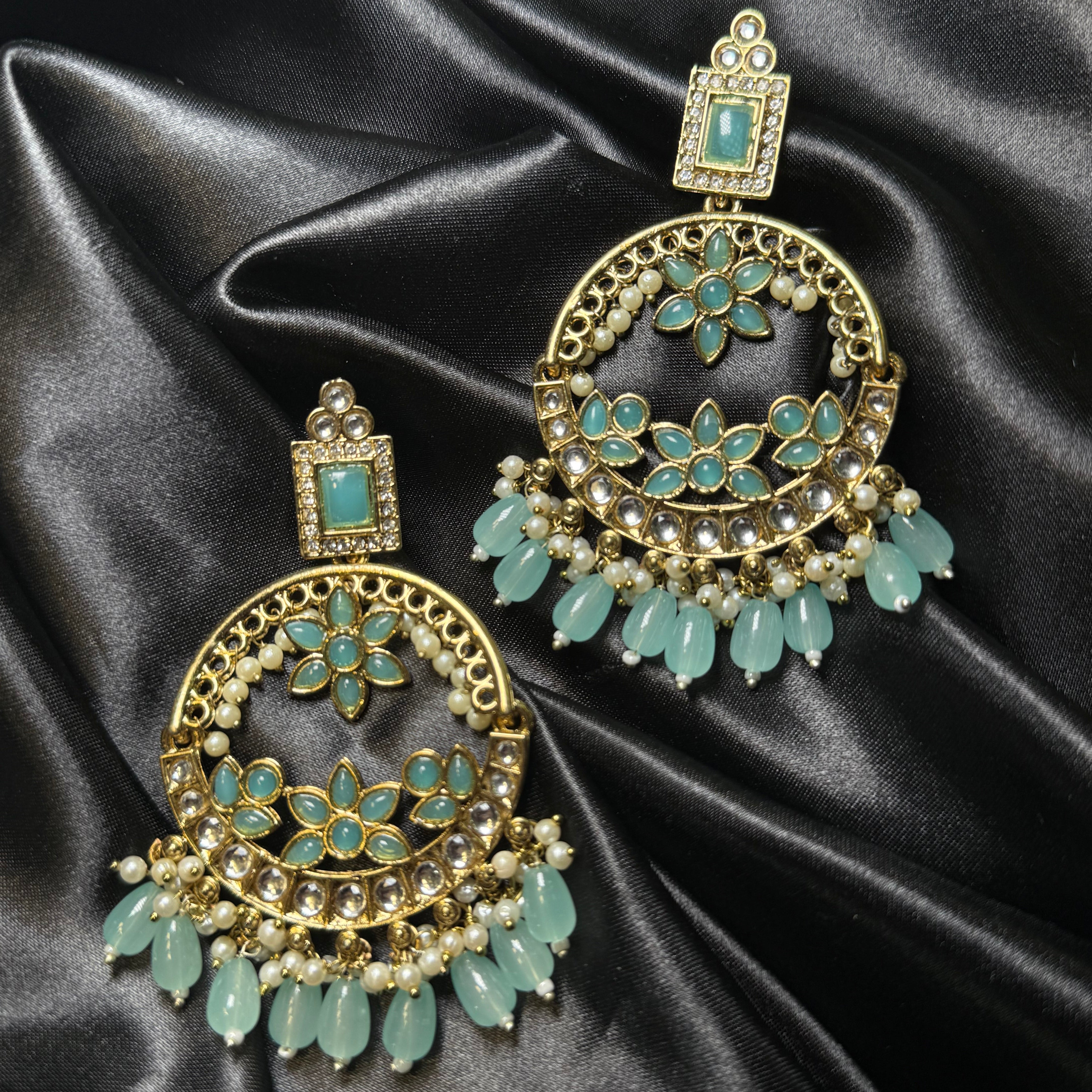 Ornate earrings with teal stones on a black satin background
