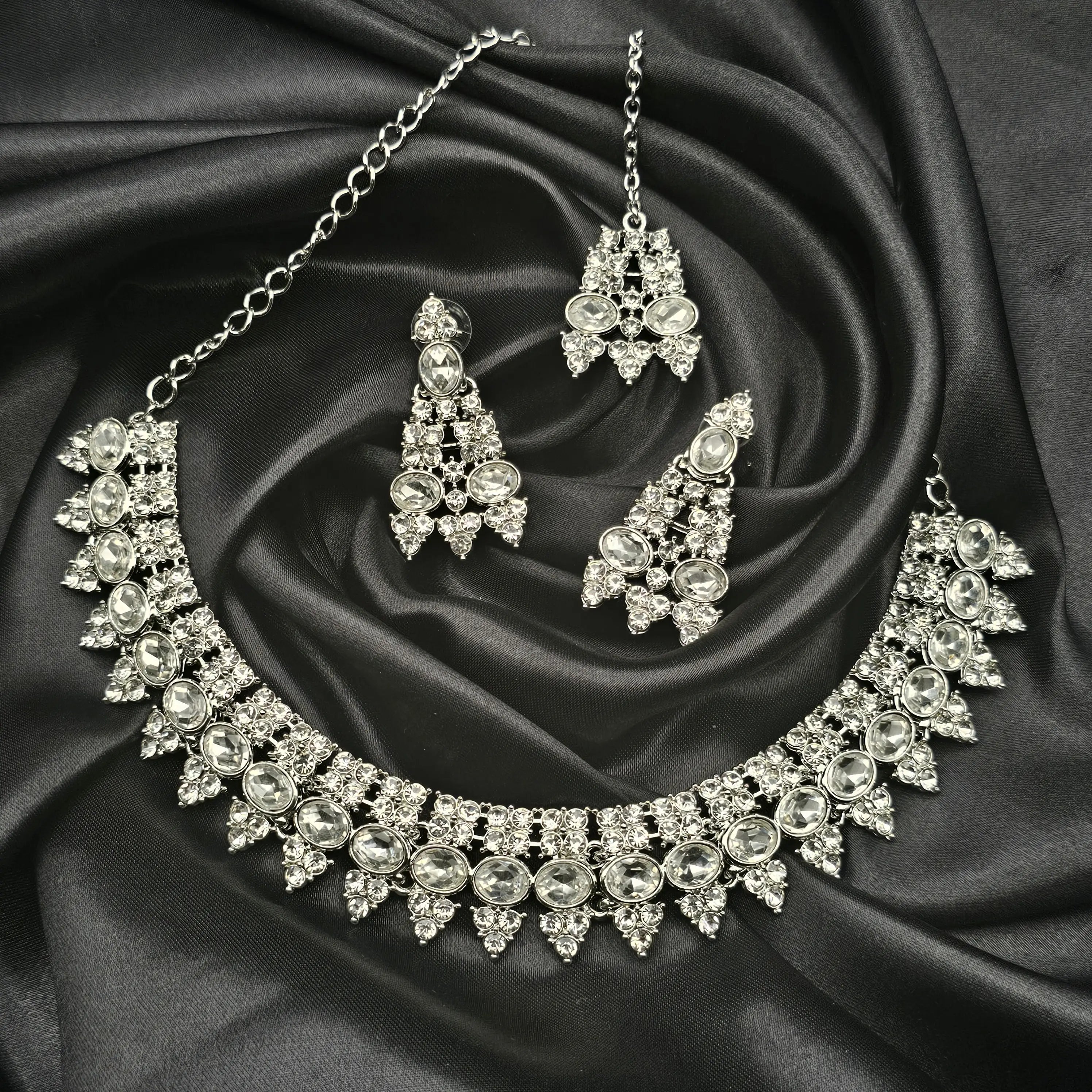 Bow Necklace Set displayed on black silk background, featuring silver-toned choker, matching earrings, and tikka with oval-cut CZ stones