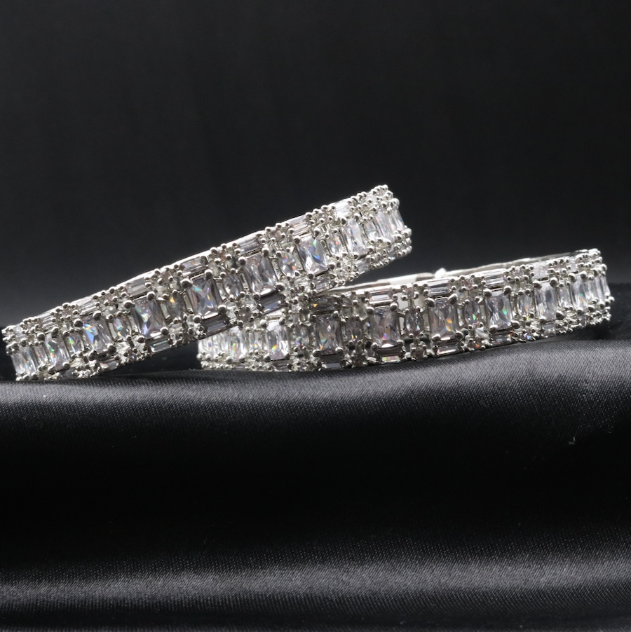 This image displays a pair of elegant castle-themed bangles. Each bangle is adorned with sparkling clear gemstones set in a meticulously crafted metal frame, showcasing a pattern that resembles a castle wall.