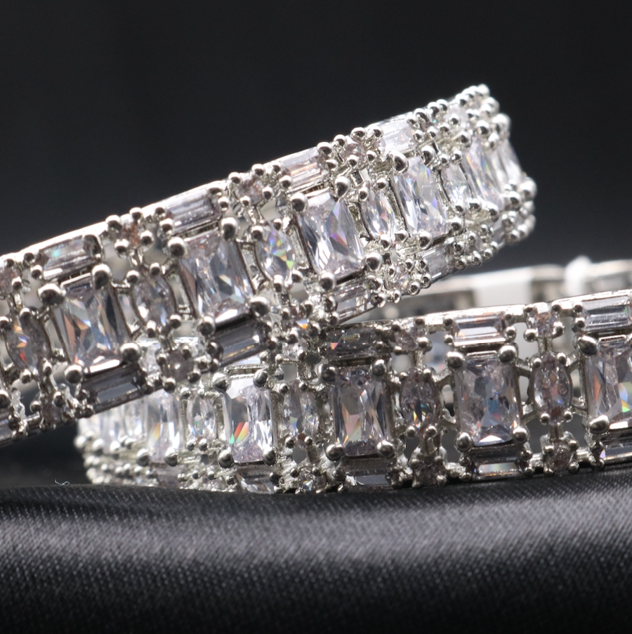 closer view of a pair of elegant castle-themed bangles. Each bangle is adorned with sparkling clear gemstones set in a meticulously crafted metal frame, showcasing a pattern that resembles a castle wall.