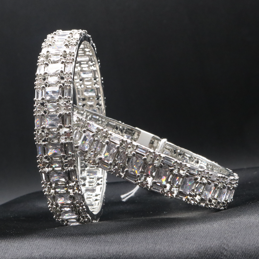 A pair of elegant castle-themed bangles. Each bangle is adorned with sparkling clear gemstones set in a meticulously crafted metal frame, showcasing a pattern that resembles a castle wall.