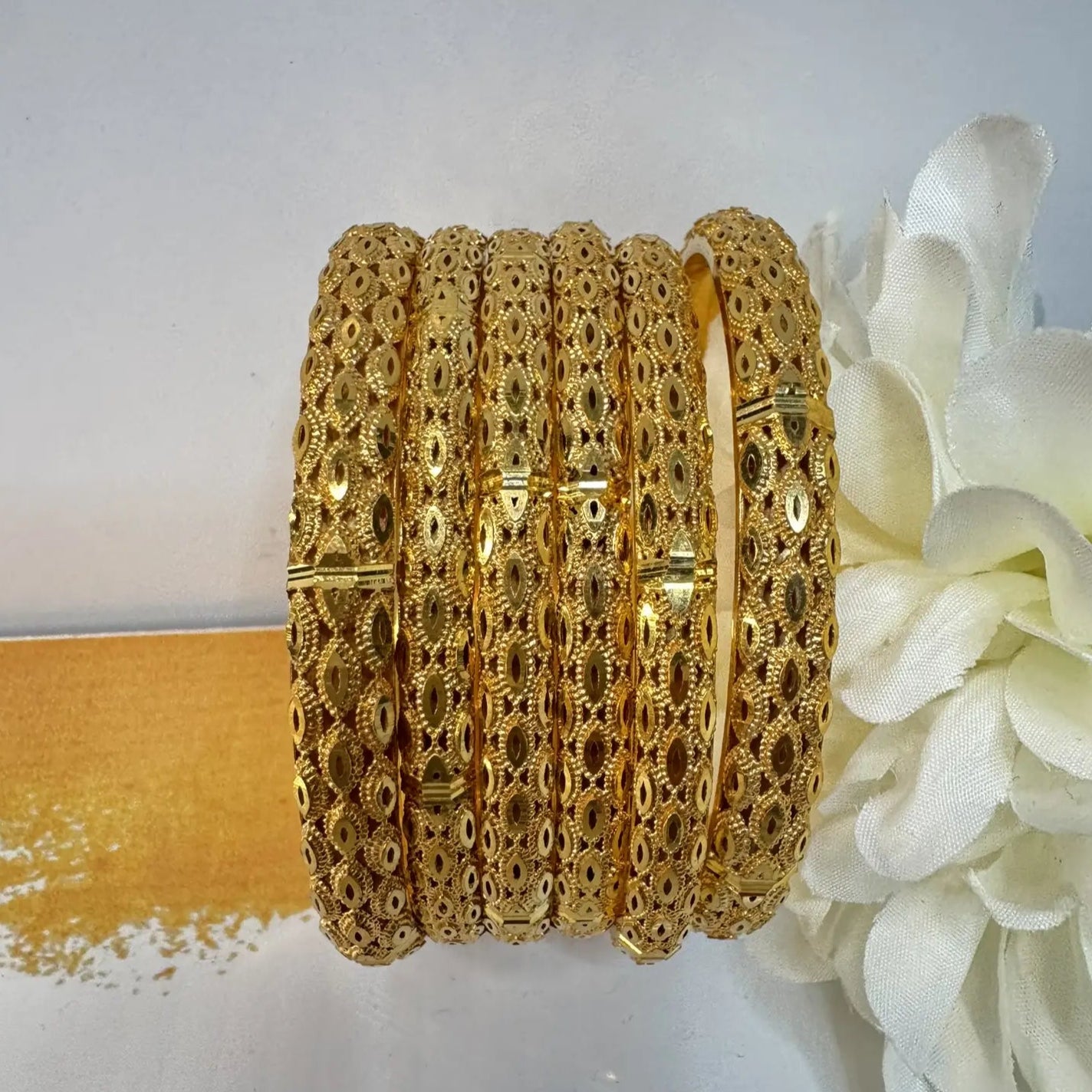 Set of six 22k gold plated bangles with a white flower on a light gray background