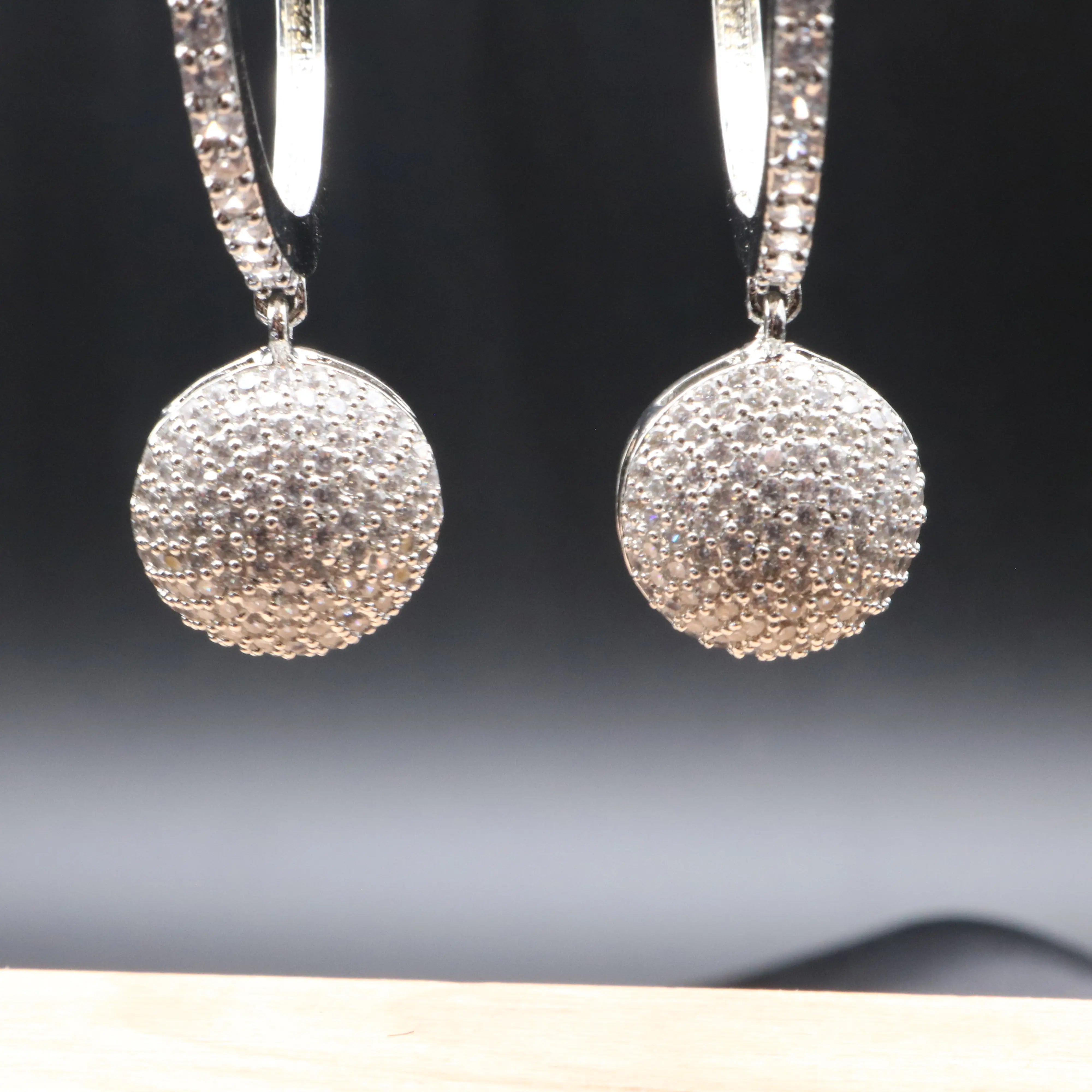 bottom part of silver hoop earrings with round puffed silver nano zircons on a dark background