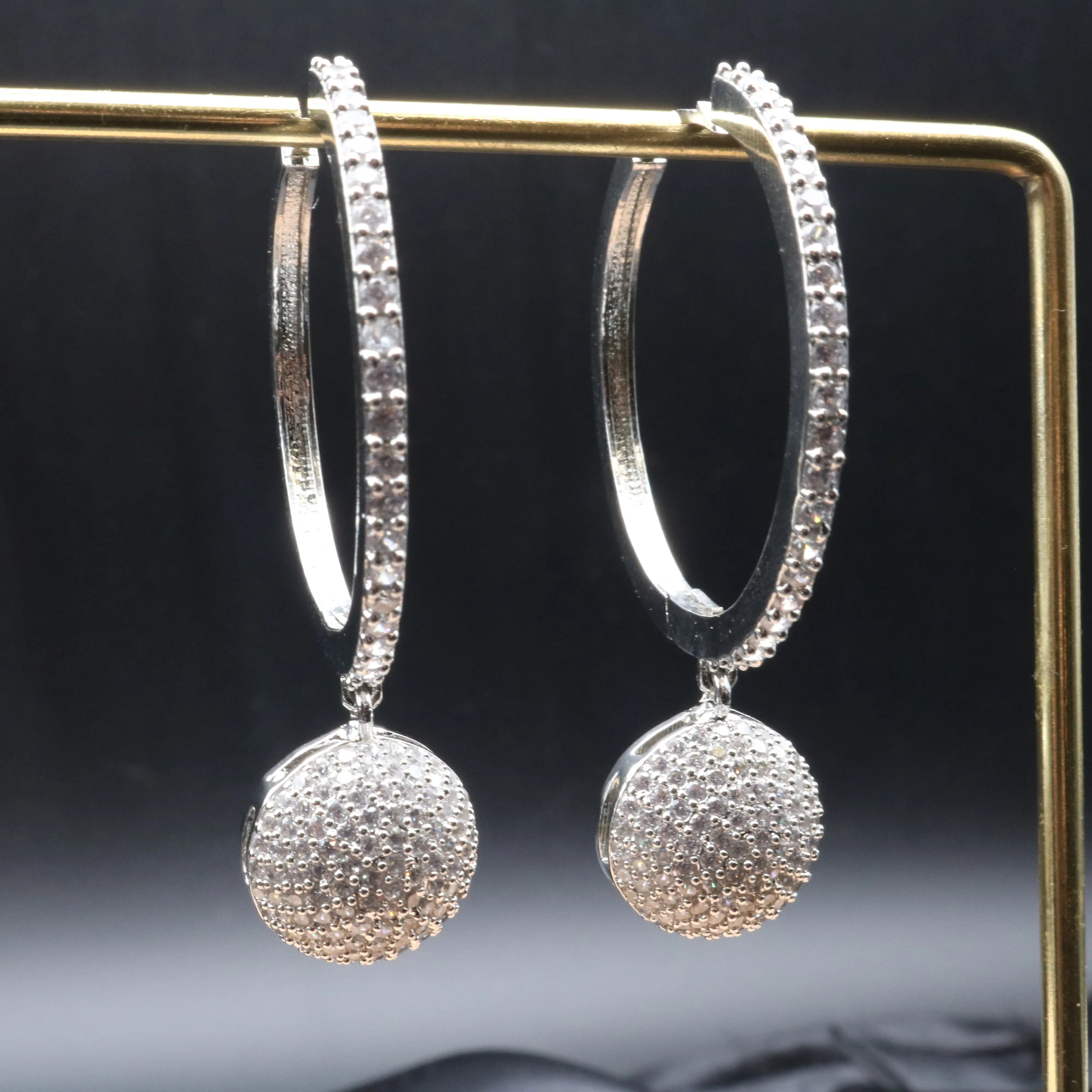 Silver hoop earrings with round puffed silver nano zircons on a dark background