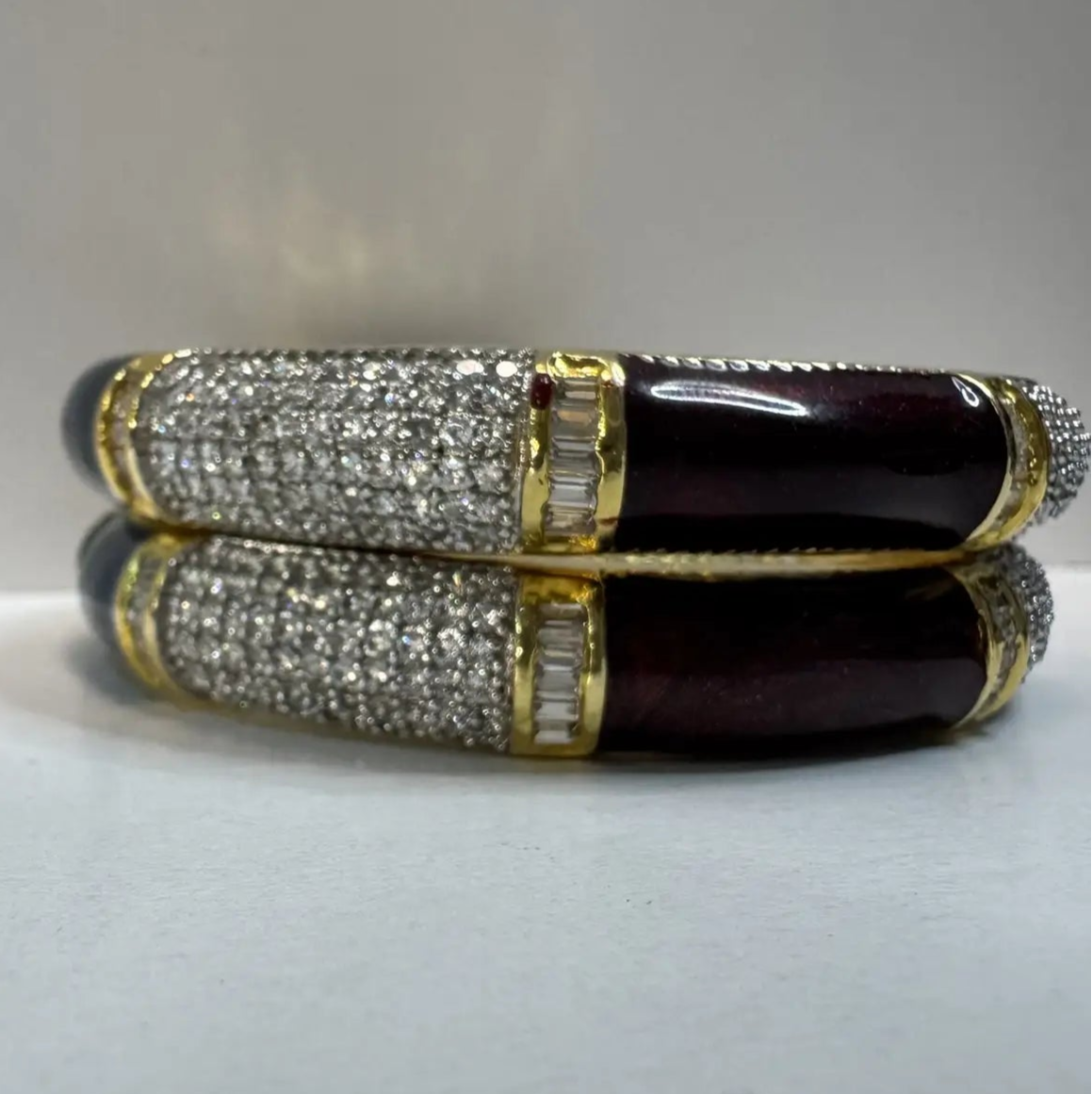 closer view of two bangles with American diamonds and green and maroon solid blocks with gemstones on a light gray background