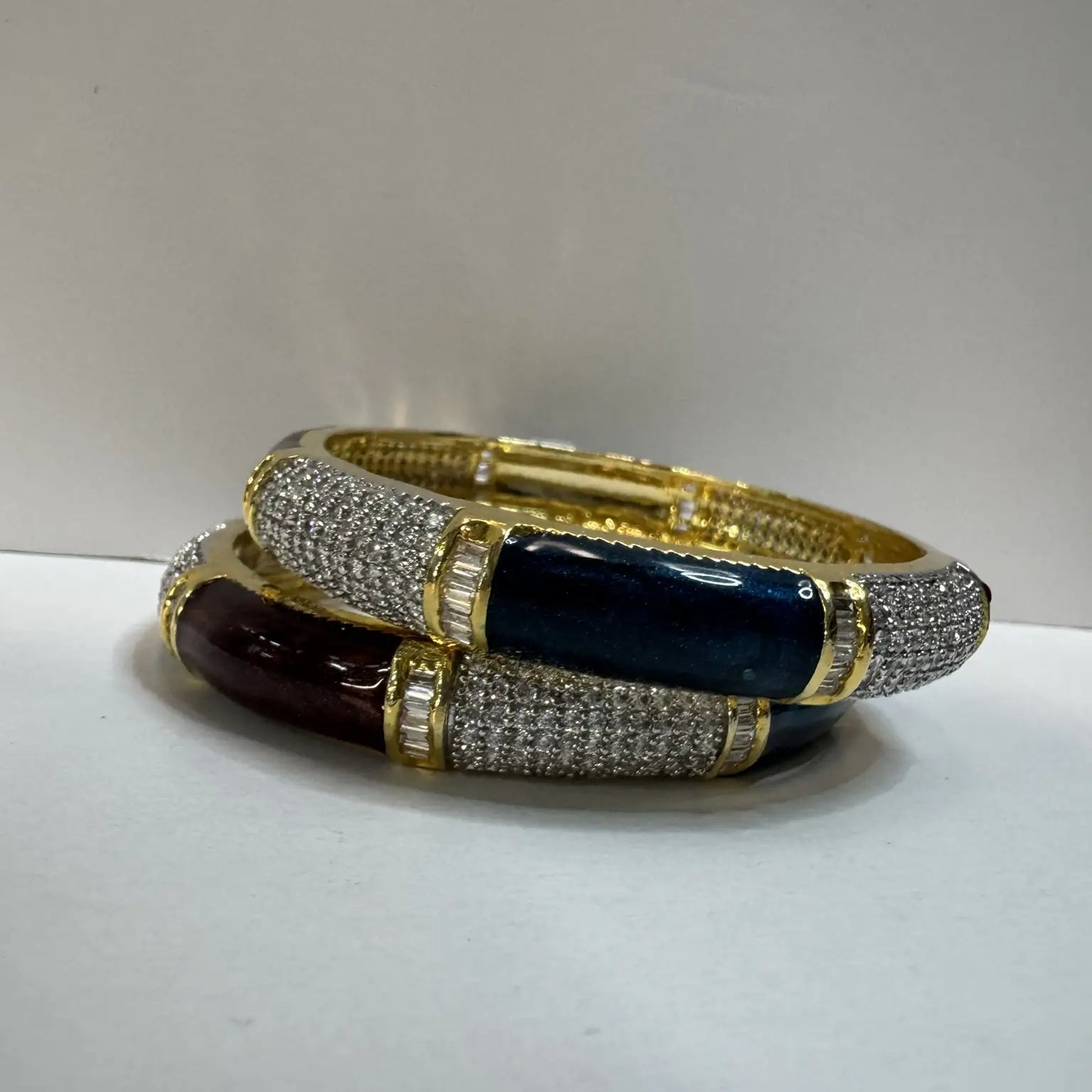 Two gold, green and maroon bangles on a white surface