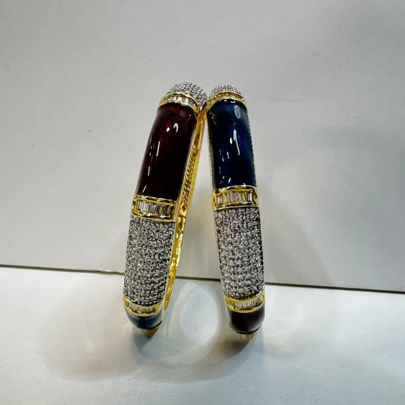 Two standing bangles with American diamonds and green and maroon solid blocks with gemstones on a light gray background