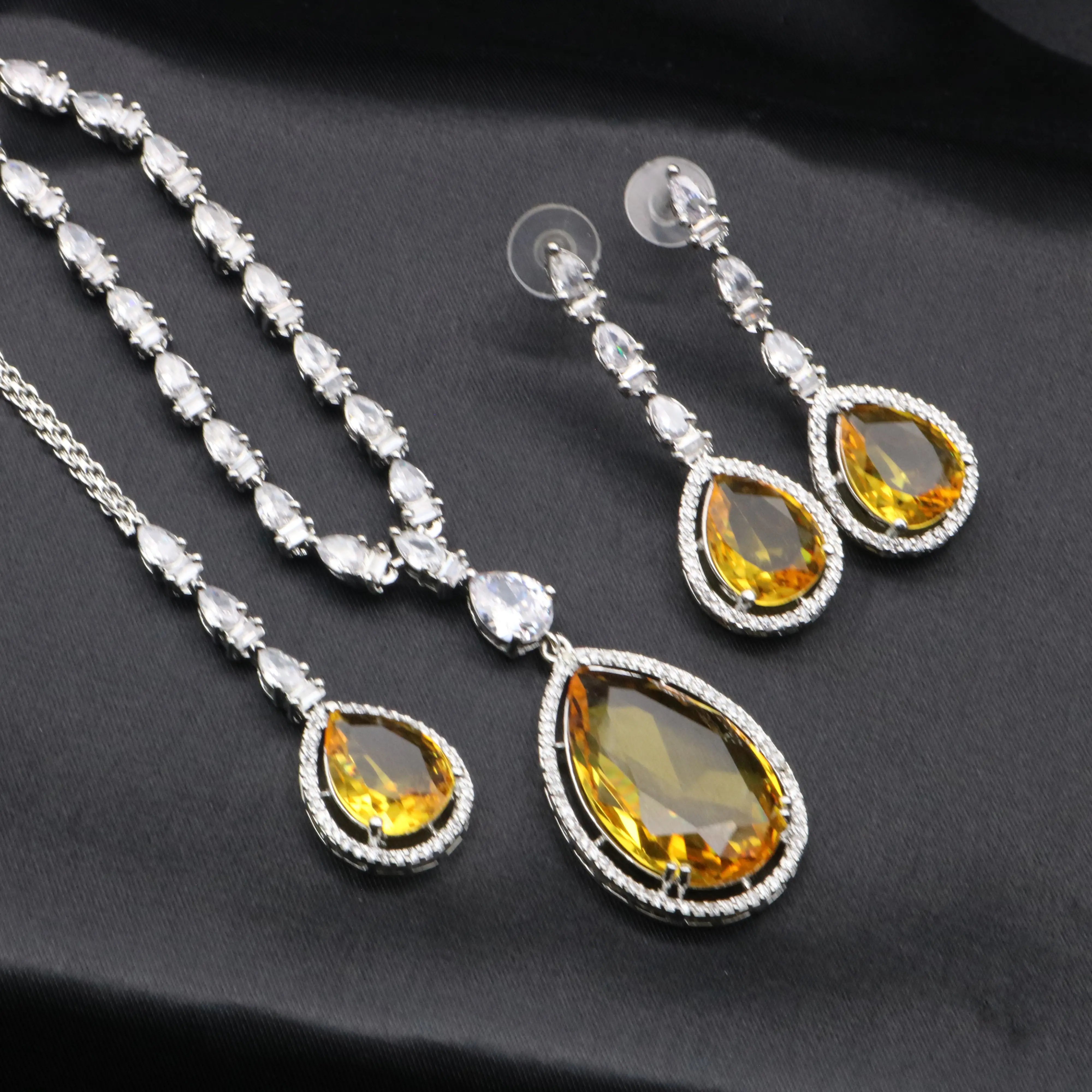 Yellow gemstone Chaos necklace and earring set with CZ stones on silver-tone base, placed on black fabric.