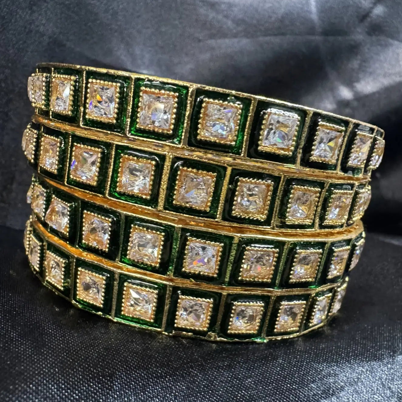 Gold and green, gold-plated bangles with square clear gemstones on a dark fabric background