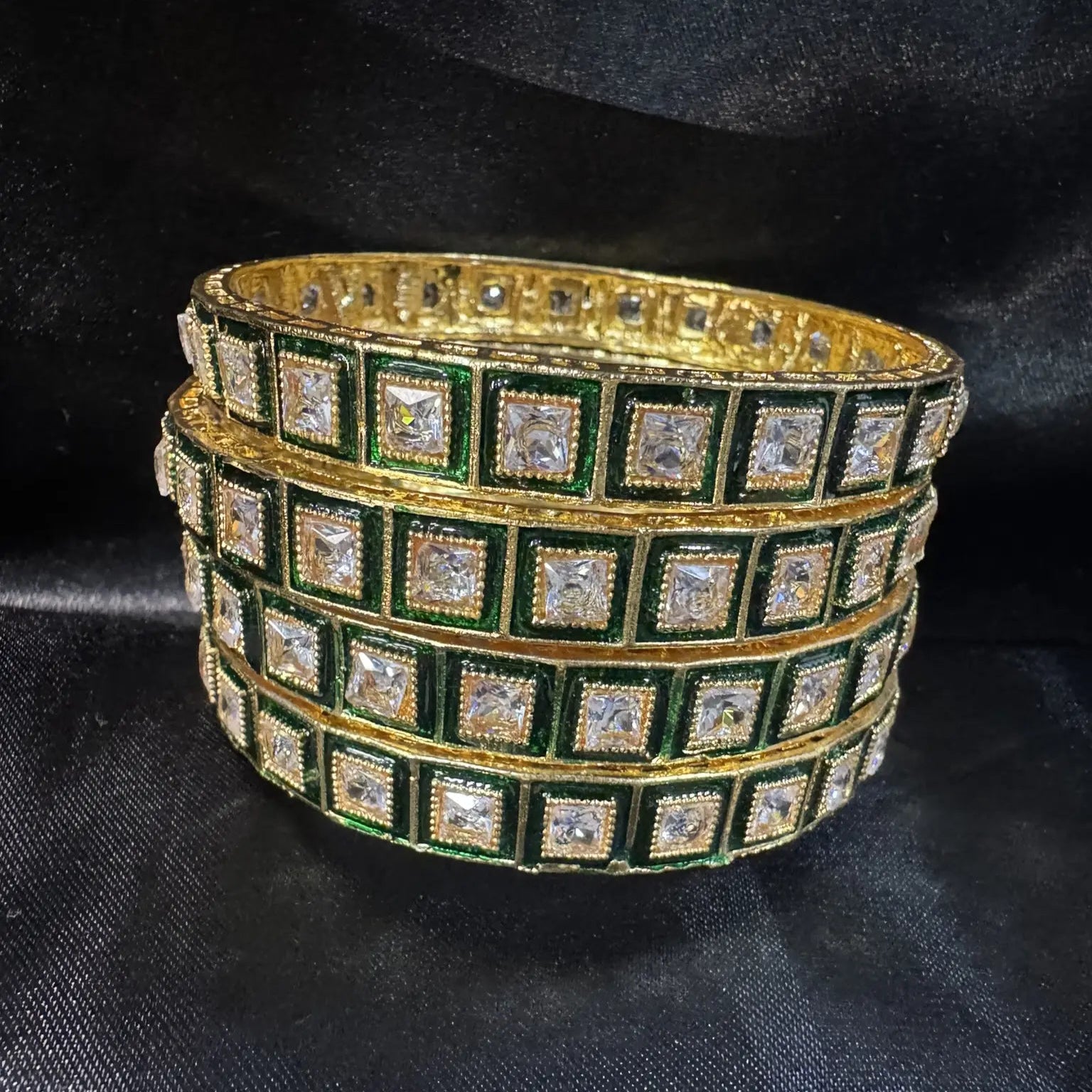 Green and gold, gold-plated bangles with square gemstones on a dark fabric background