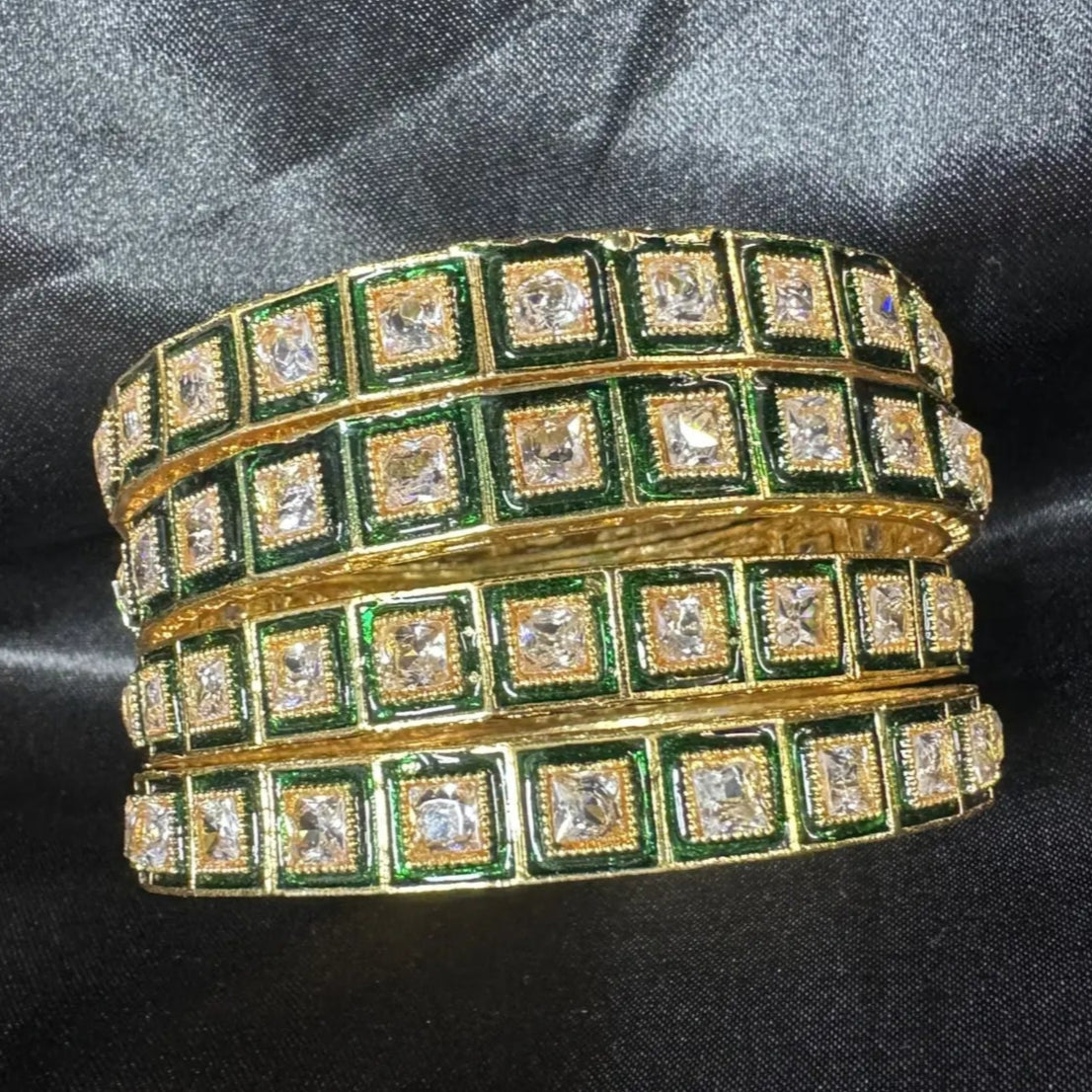 Gold and green bangles with square clear gemstones on a black fabric background