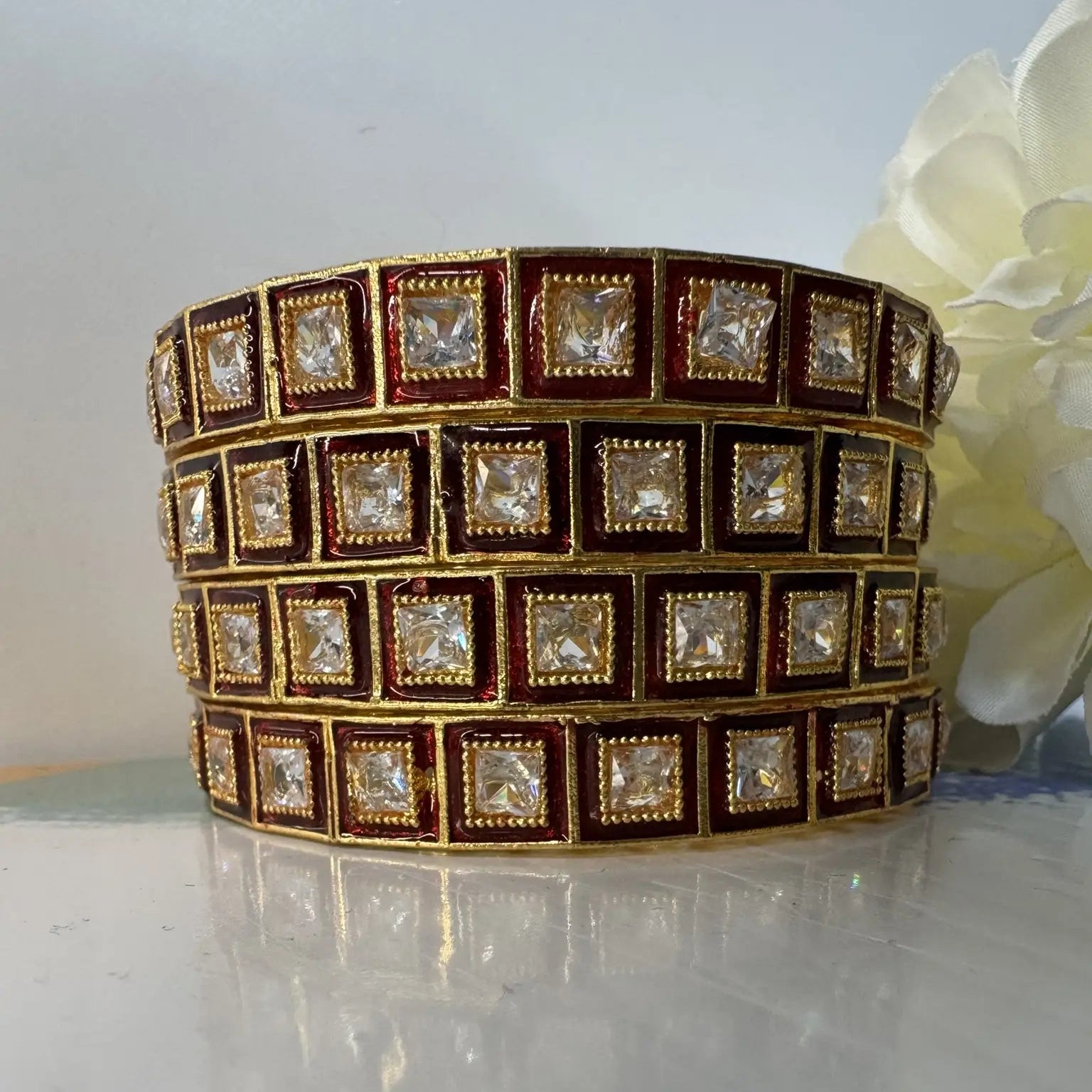 Red and gold, gold-plated bangles with square gemstones on a reflective surface