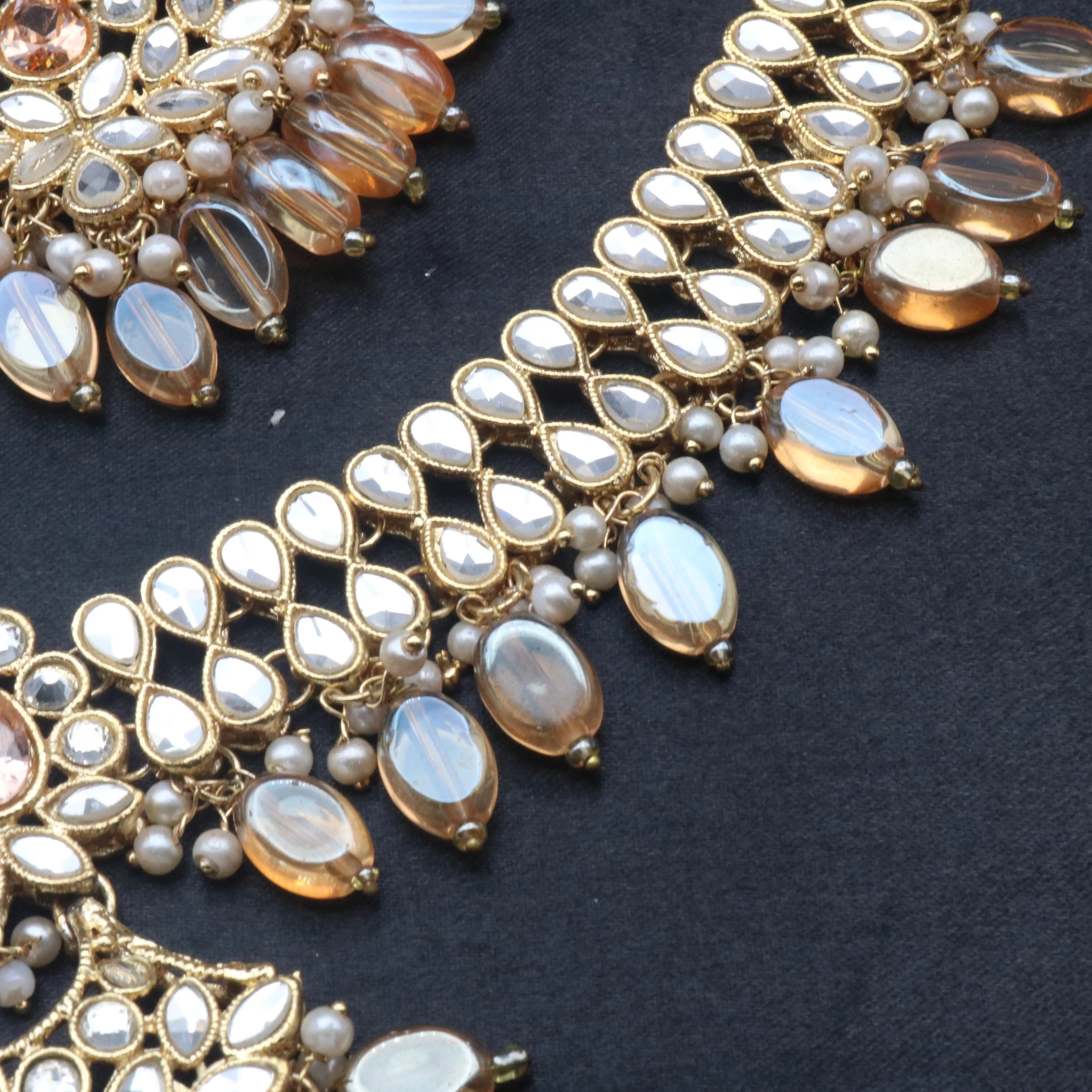 Close-up of Coral kundan necklace showcasing mirror-cut stones and champagne beads on black fabric