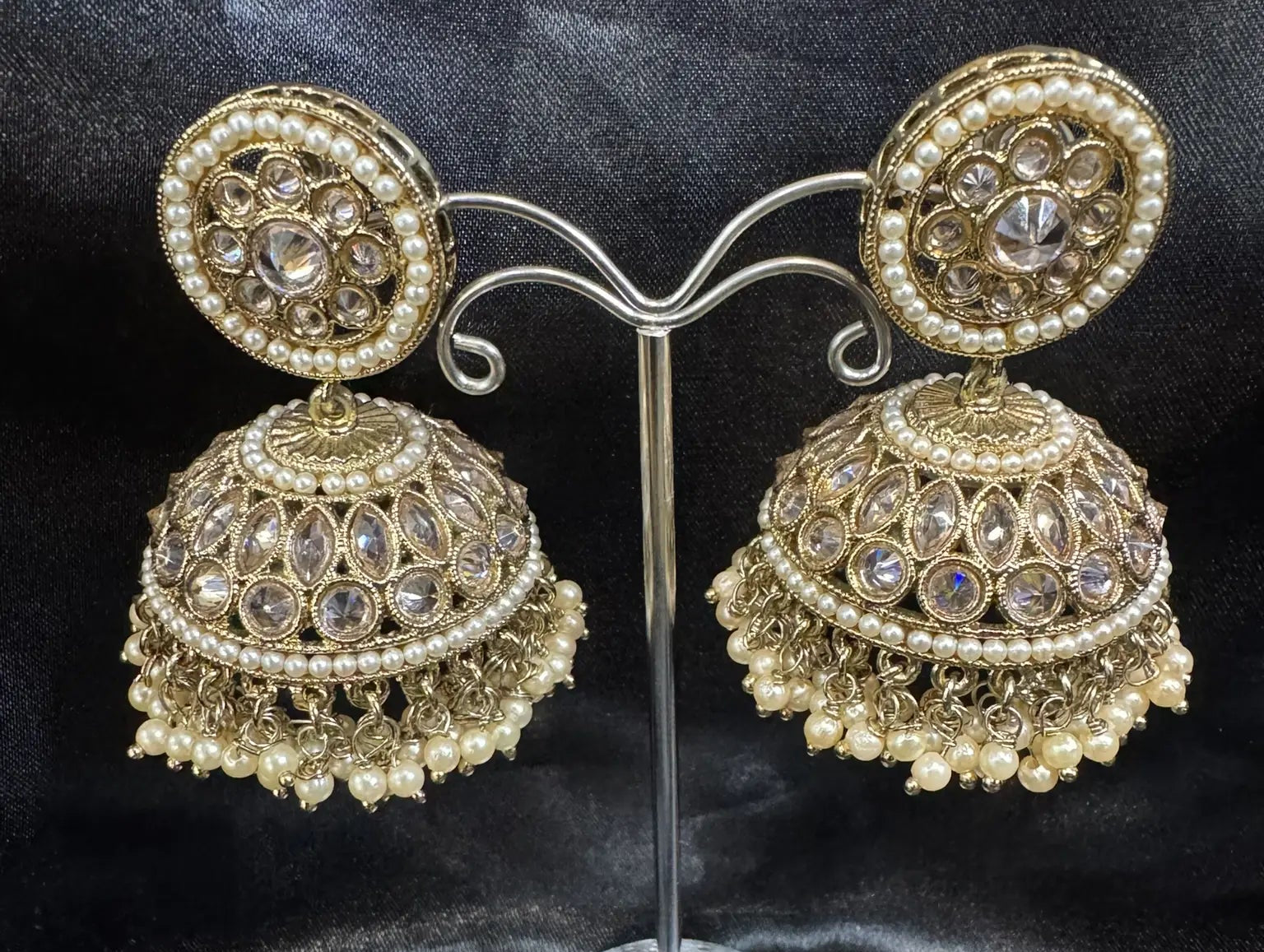 Pair of gold and pearl Jhumka earrings on a stand against a black satin background