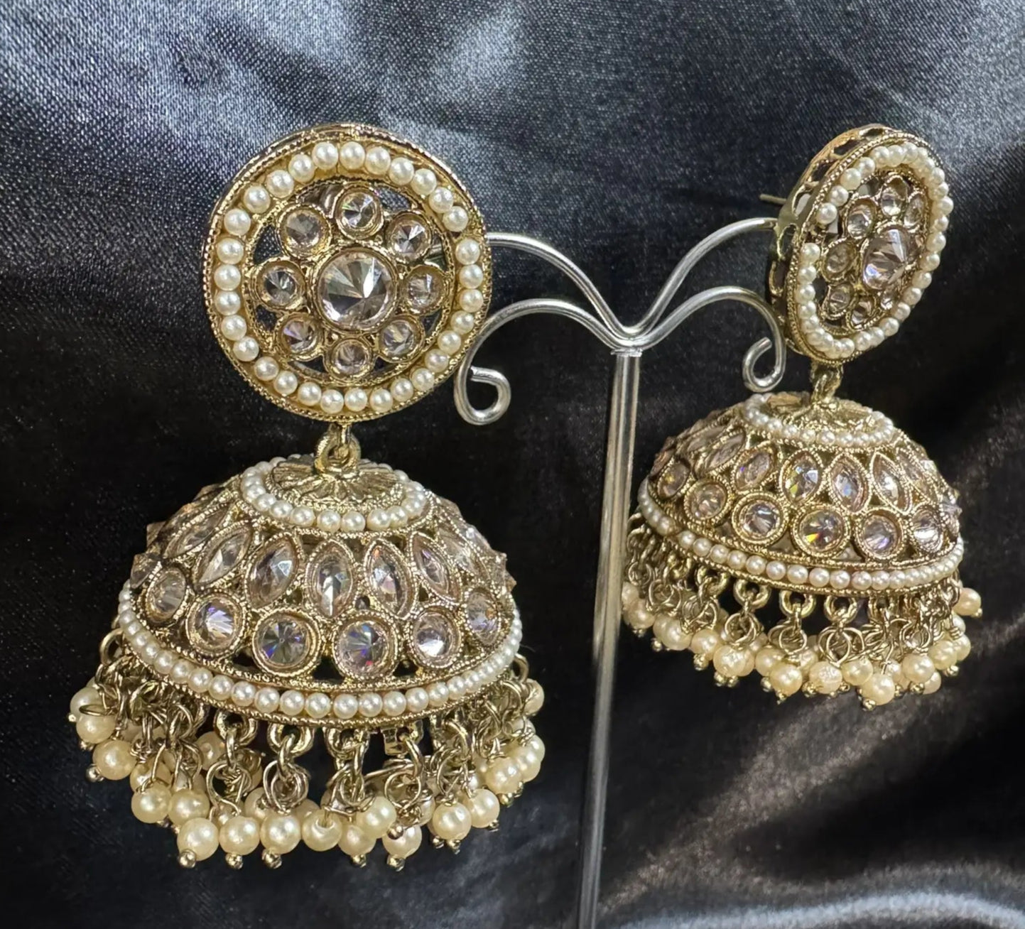 Gold and pearl jhumka earrings on a stand against a dark fabric background
