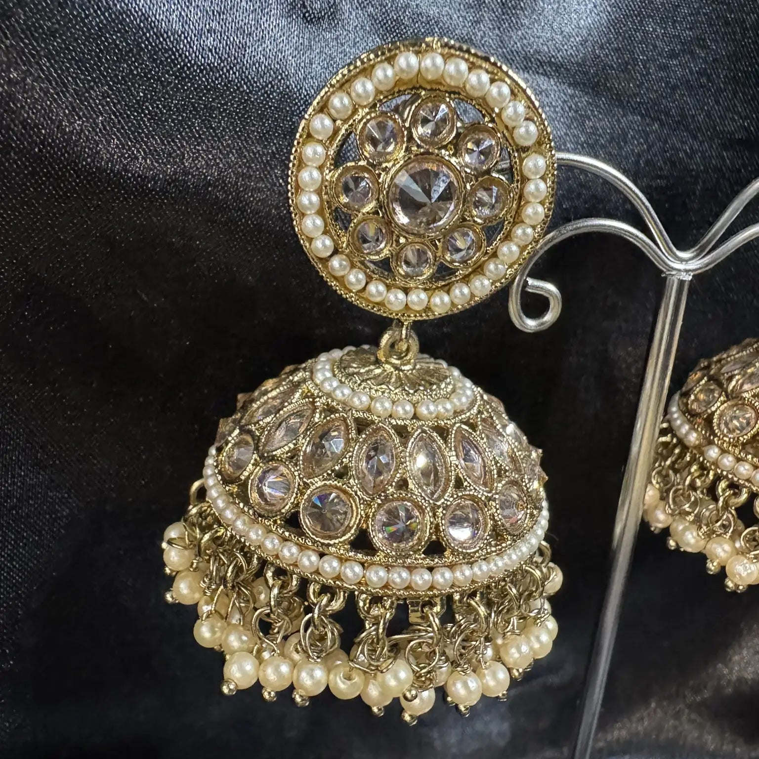 Gold and pearl jhumka earring on a dark fabric background