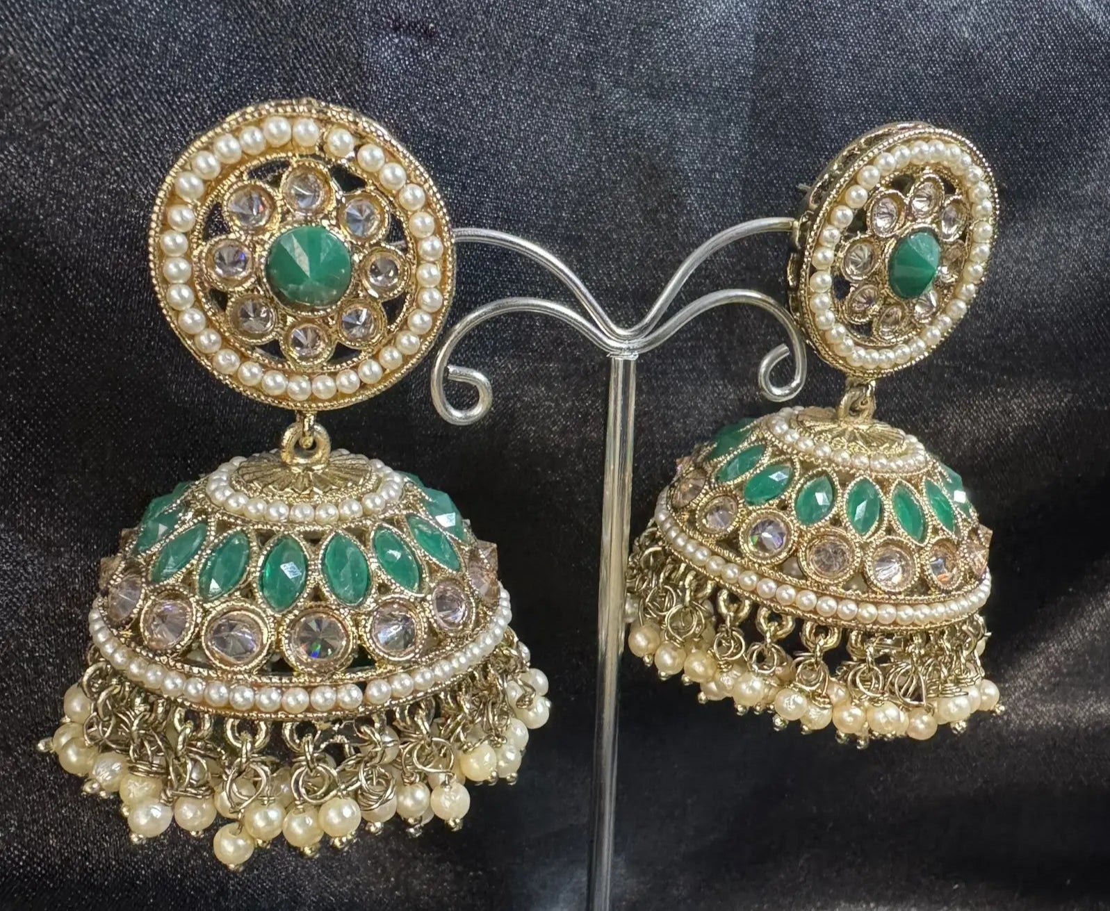 Pair of gold and green jhumkay on a stand against a dark fabric background
