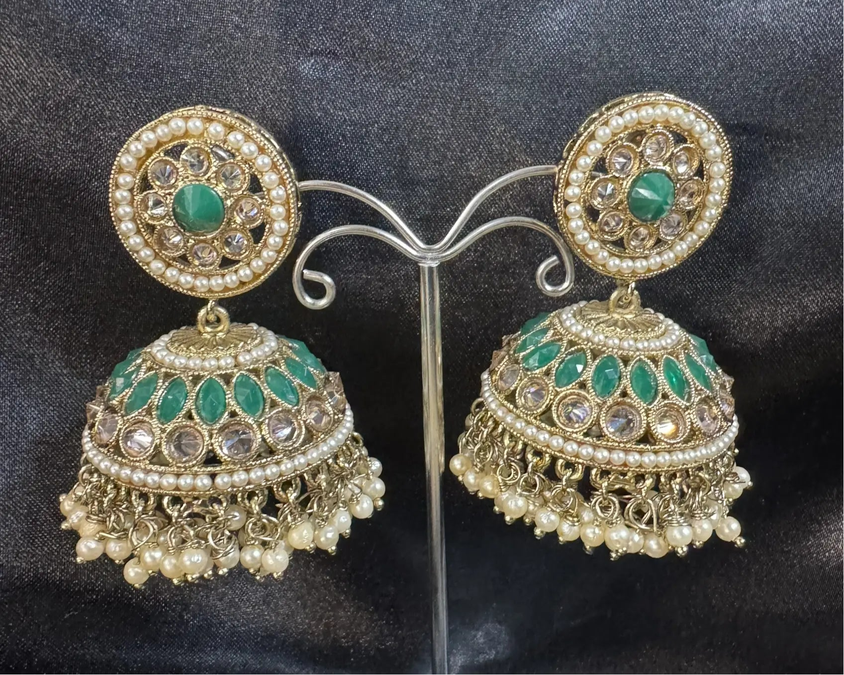 Ornate gold and green jhumkay on a dark fabric background