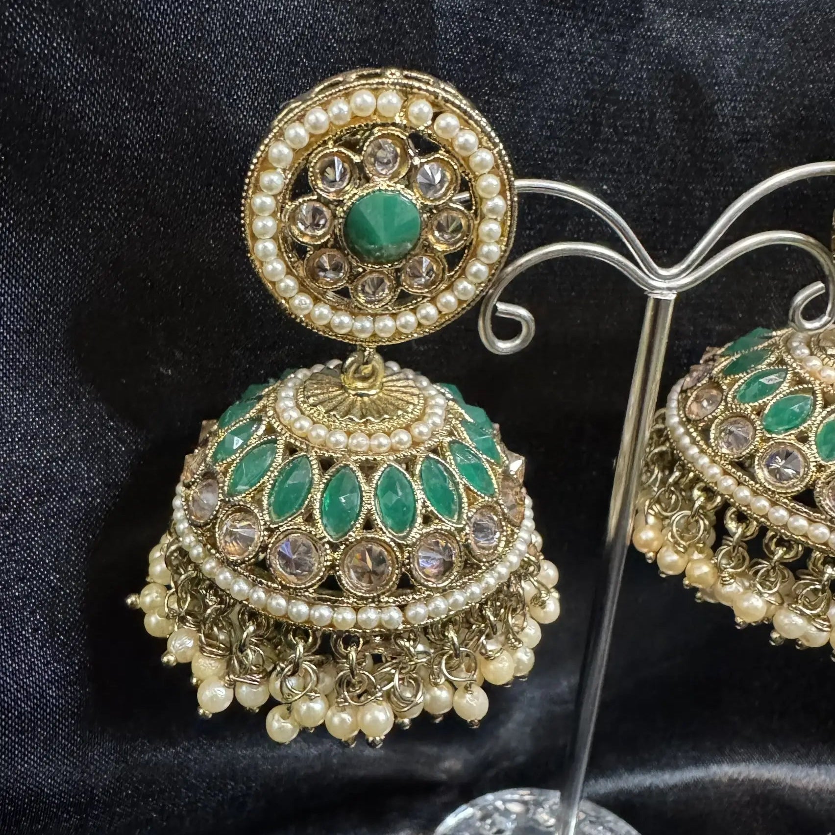 Jhumka earrings with green gemstones and pearl details on a black background