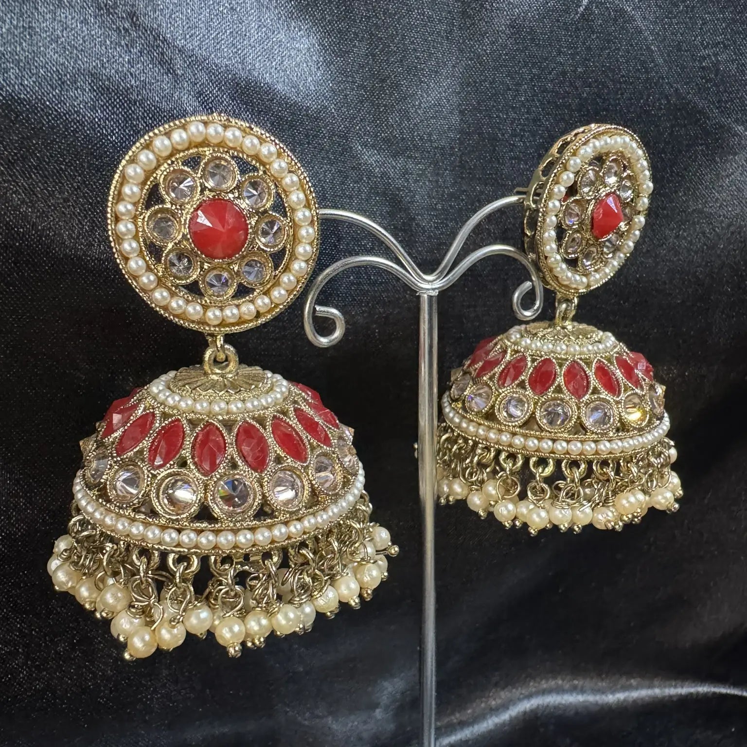 gold and red jhumka earrings on a stand against a dark background