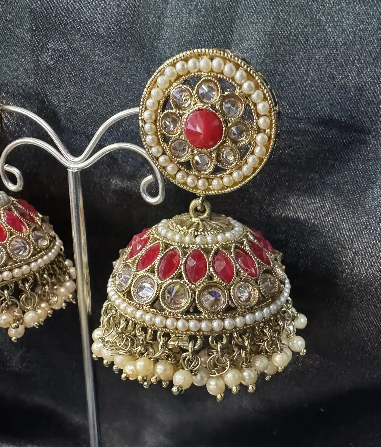 gold and red jhumka earring on a stand against a dark fabric background