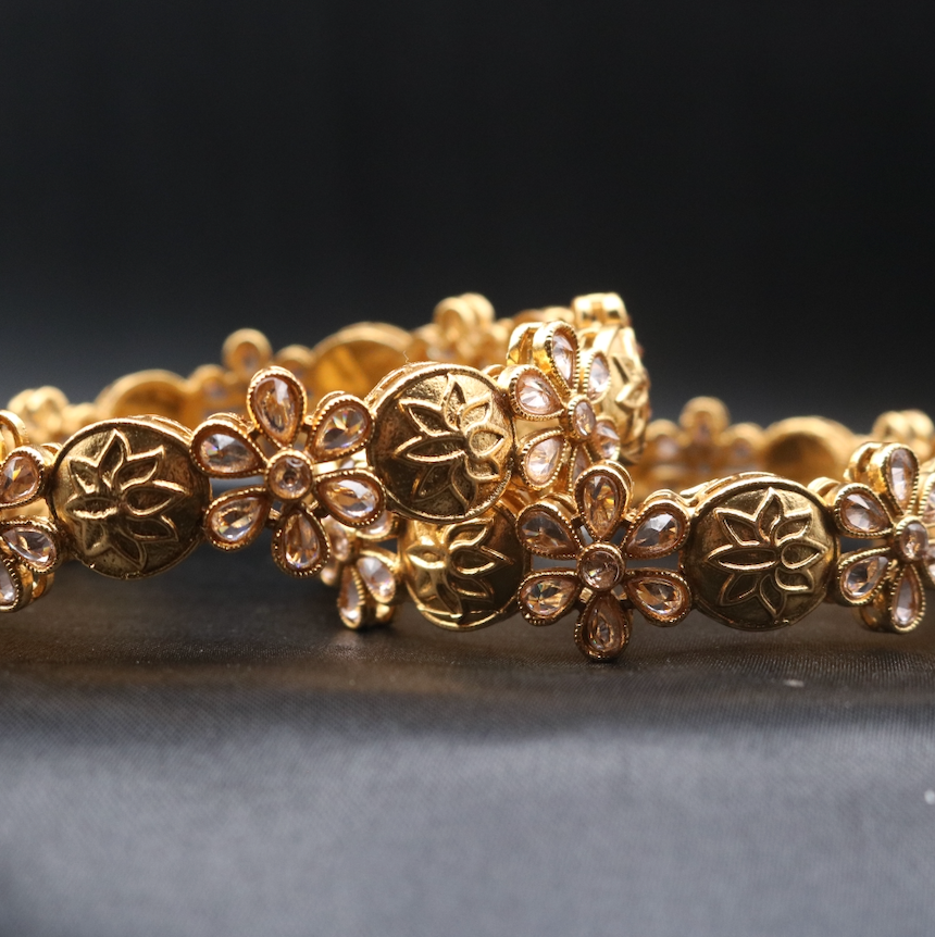 A set of two gold-plated bangles with floral patterns and star motifs.
