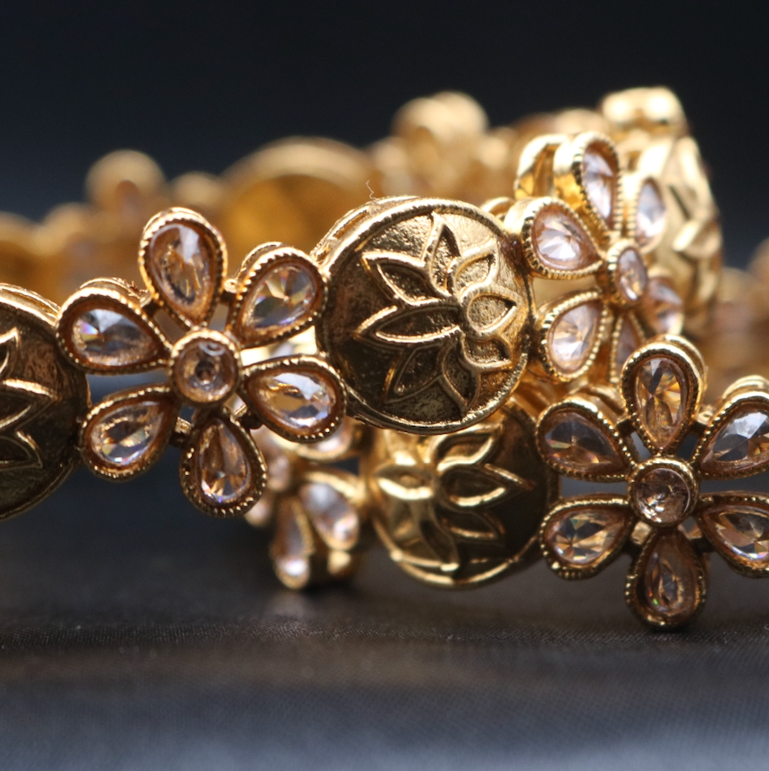 closer view of set of two gold-plated bangles with floral patterns and star motifs.