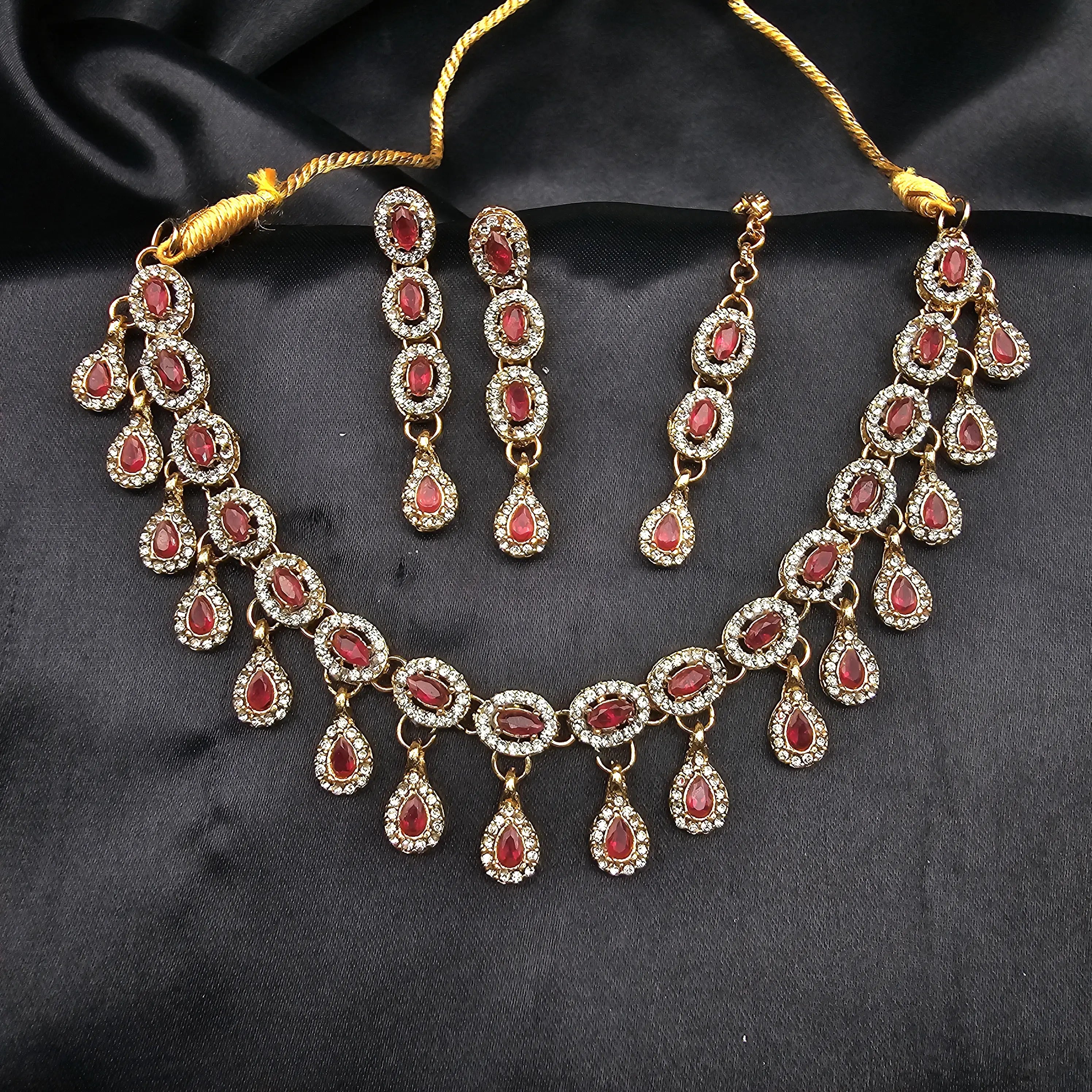Ruby red variant of the Daint necklace set with teardrop stones and gold-plated base on black fabric