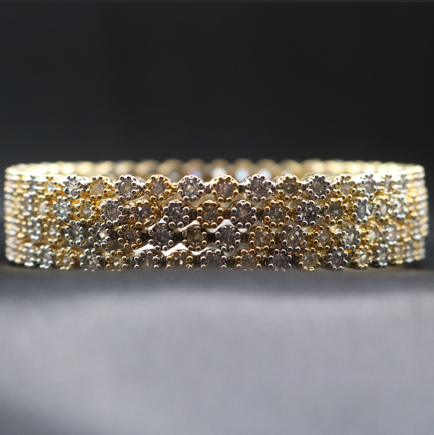 A gold-colored bangle adorned with sparkling American diamonds, displayed against a dark background.