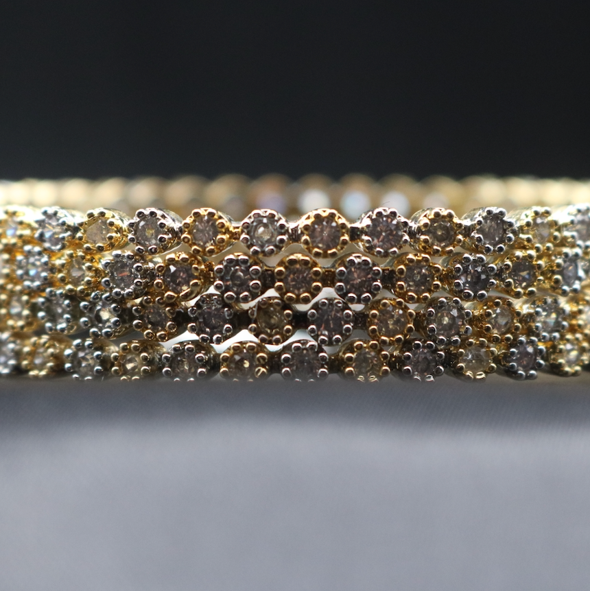 closer view of gold-colored bangle adorned with sparkling American diamonds, displayed against a dark background.