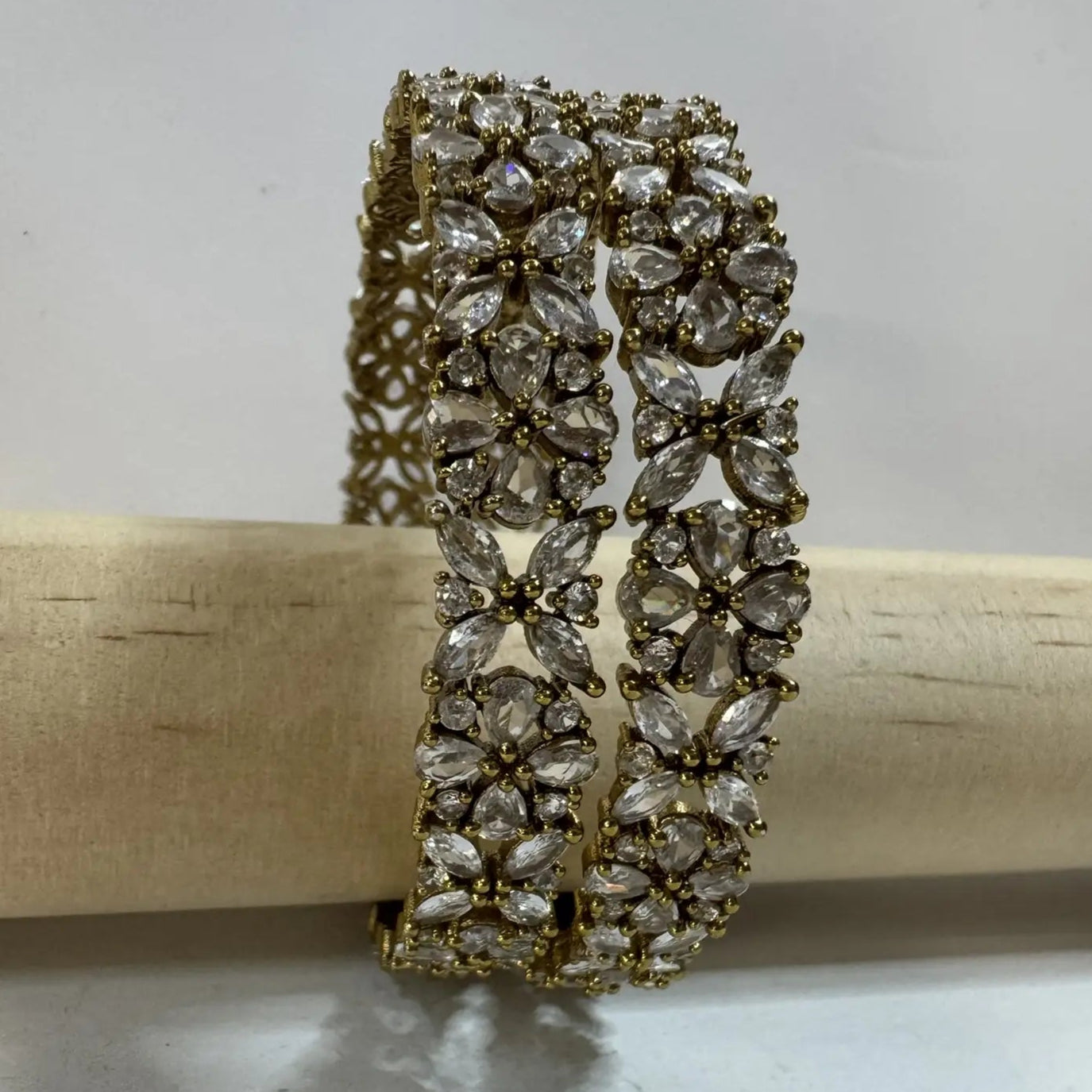 Pair of gold-plated crystal bangles on a wooden stick against a white background