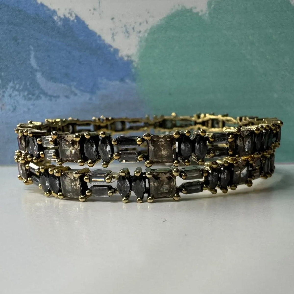 Gold plated bangles with black gemstones and gold accents on a white surface with a colorful background