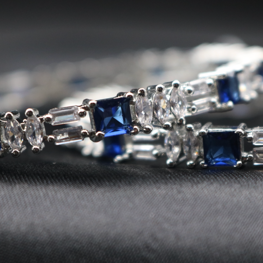 closer view of American diamonds bangles with blue gemstones and silver accents on a black surface 