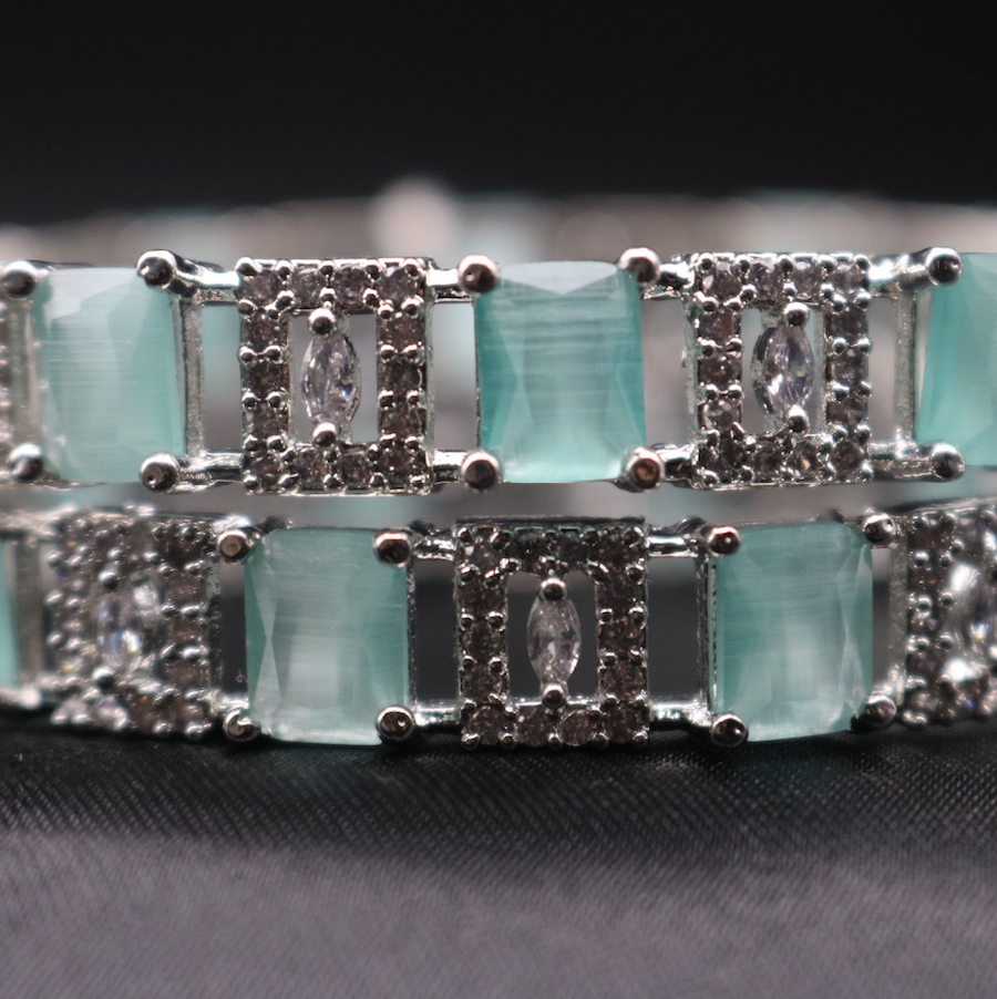 a closer look of silver bangles adorned with teal and clear stones, showcasing its sparkle and design.