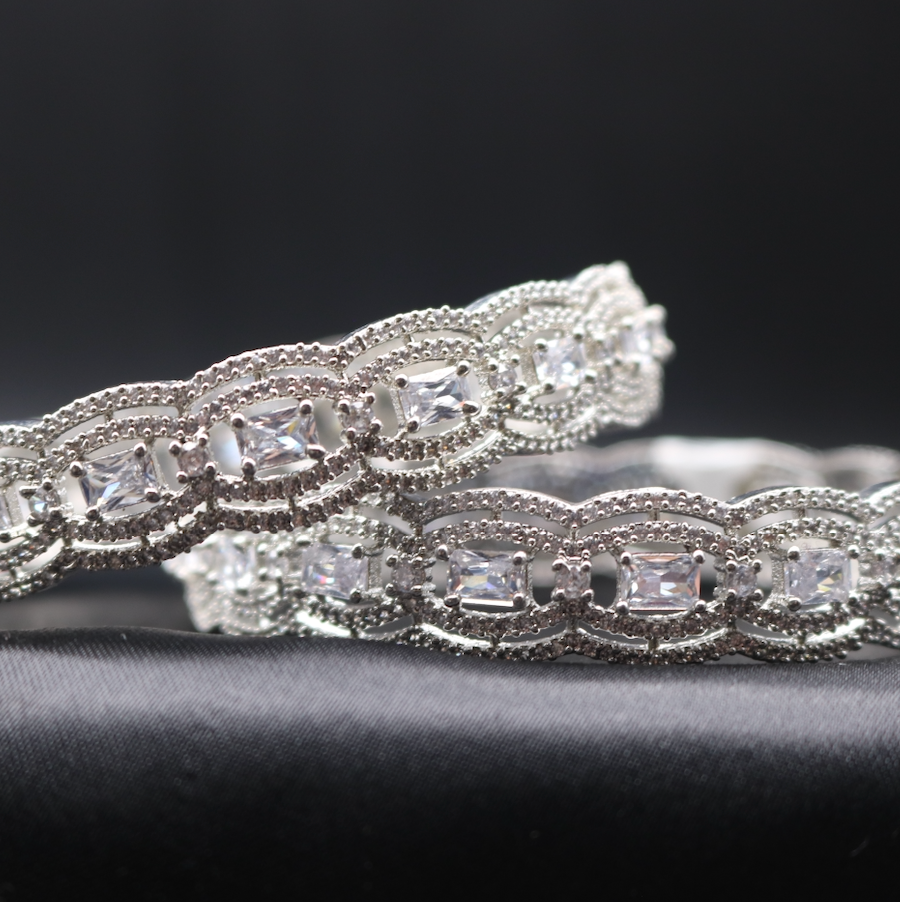 A close-up of two stainless steel bangles adorned with American diamonds, displayed against a dark background.
