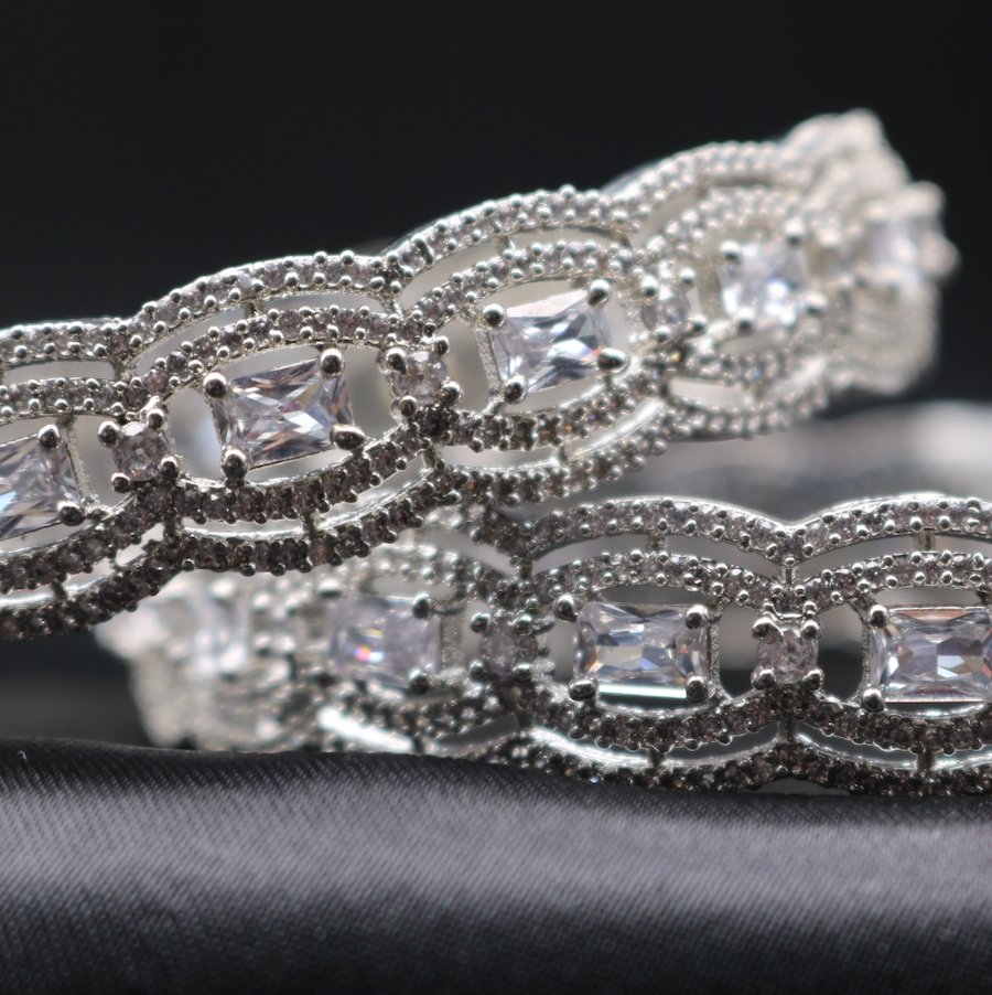 A pair of stainless steel bangles adorned with American diamonds, displayed against a dark background.
