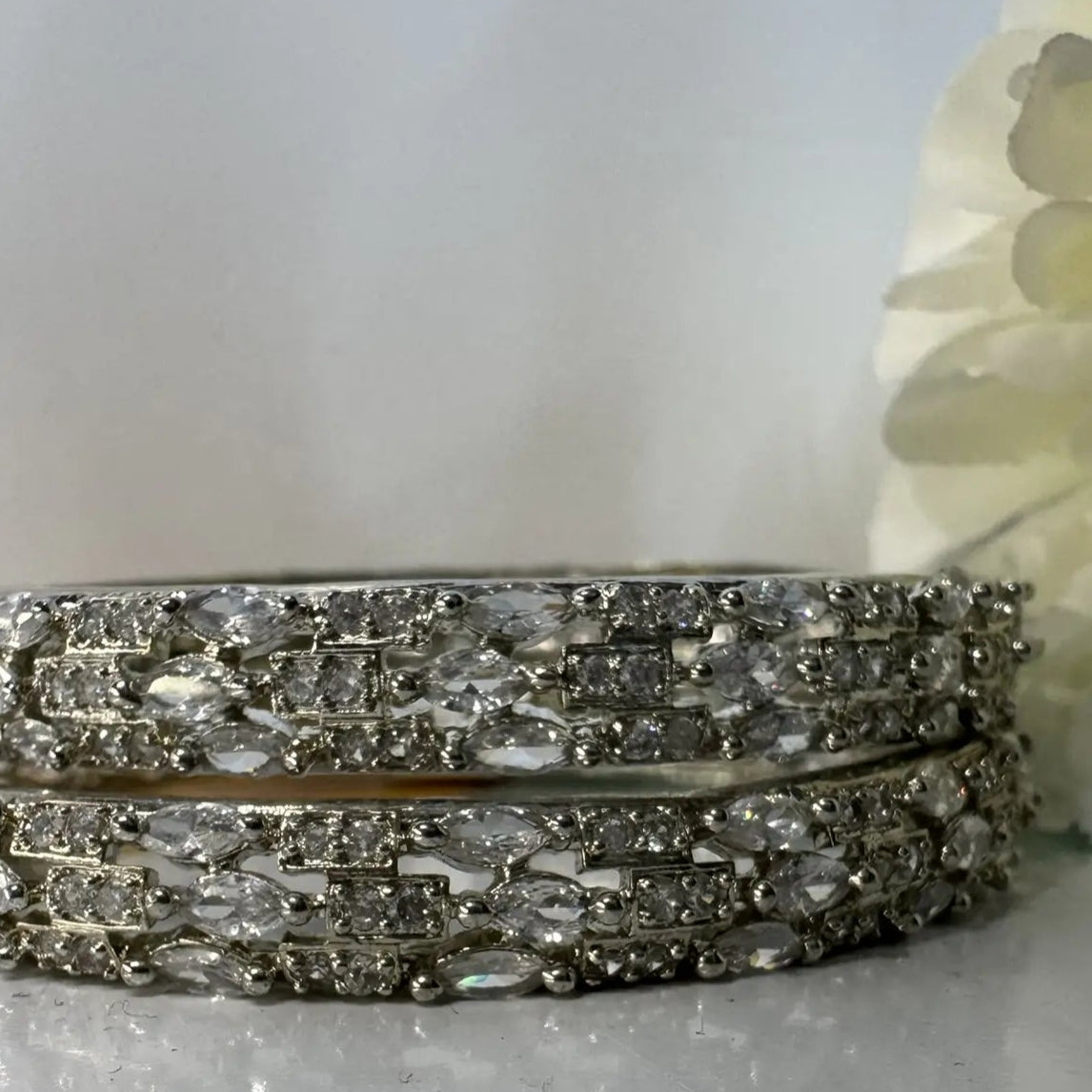 American diamonds bangles in silver with clear gemstones on a white background and white flower at the back