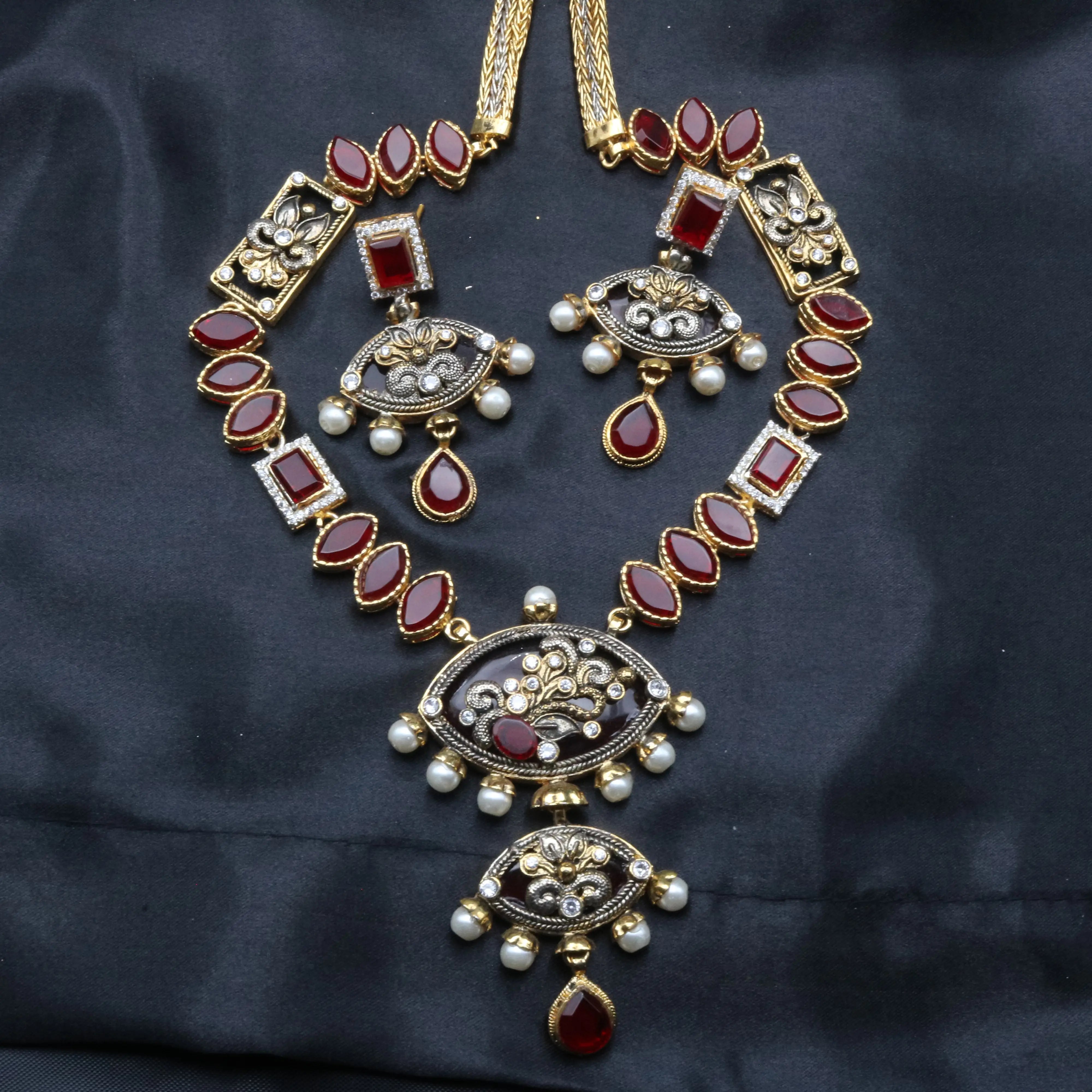Egypt necklace and earrings set laid flat with oval ruby stones, intricate detailing, and pearls.