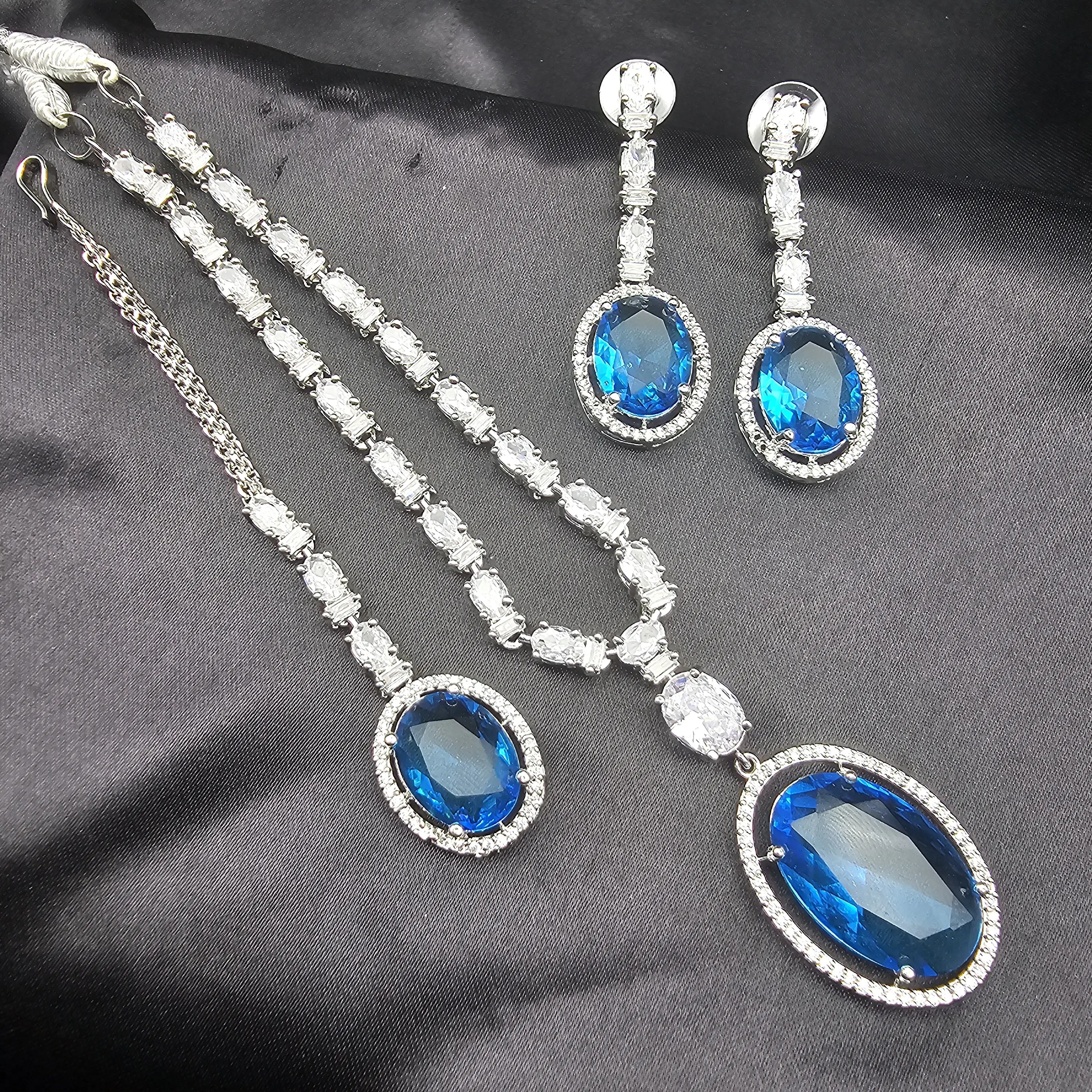 Enchant Necklace Set in Sapphire Blue CZ displayed on black fabric, showcasing deep blue gemstone-inspired center stones with silver-tone setting and earrings