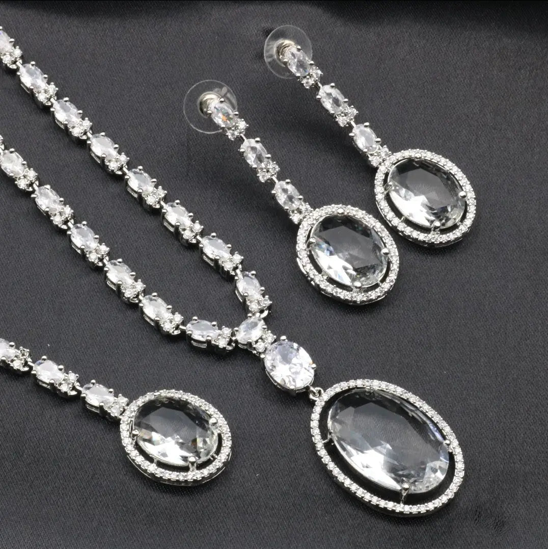 Enchant Necklace Set in Clear CZ displayed on black fabric, featuring oval crystal stones with pavé detailing and matching earrings