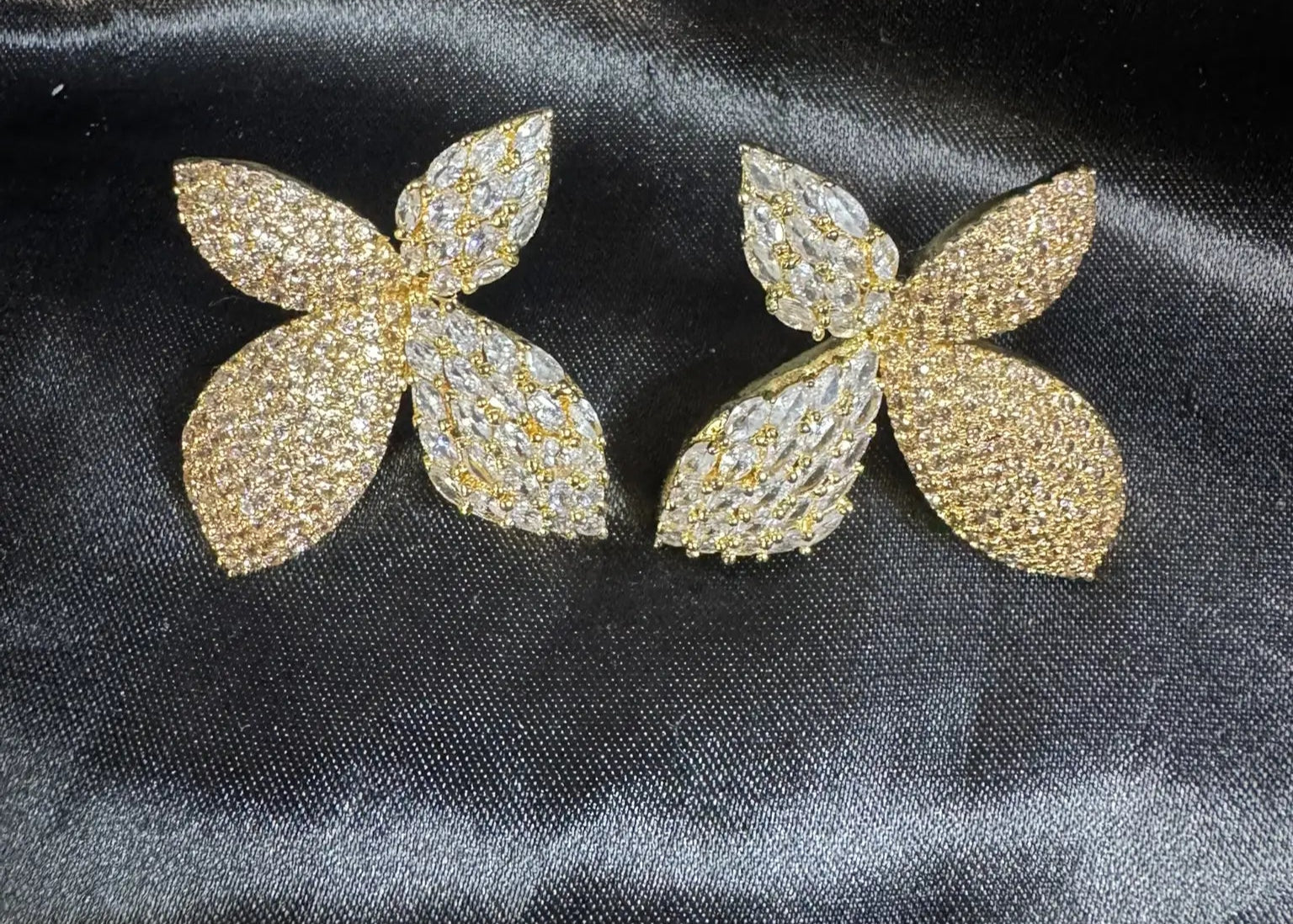Pair of gold butterfly-shaped earrings on a black satin background