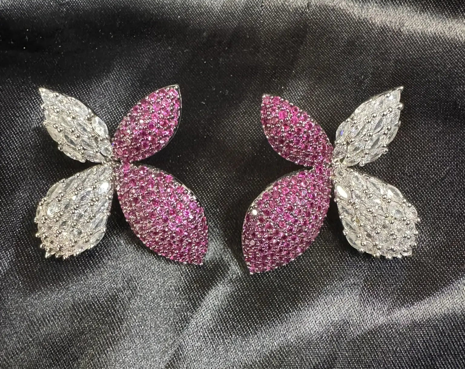 Pair of pink and silver butterfly-shaped earrings on a black satin background