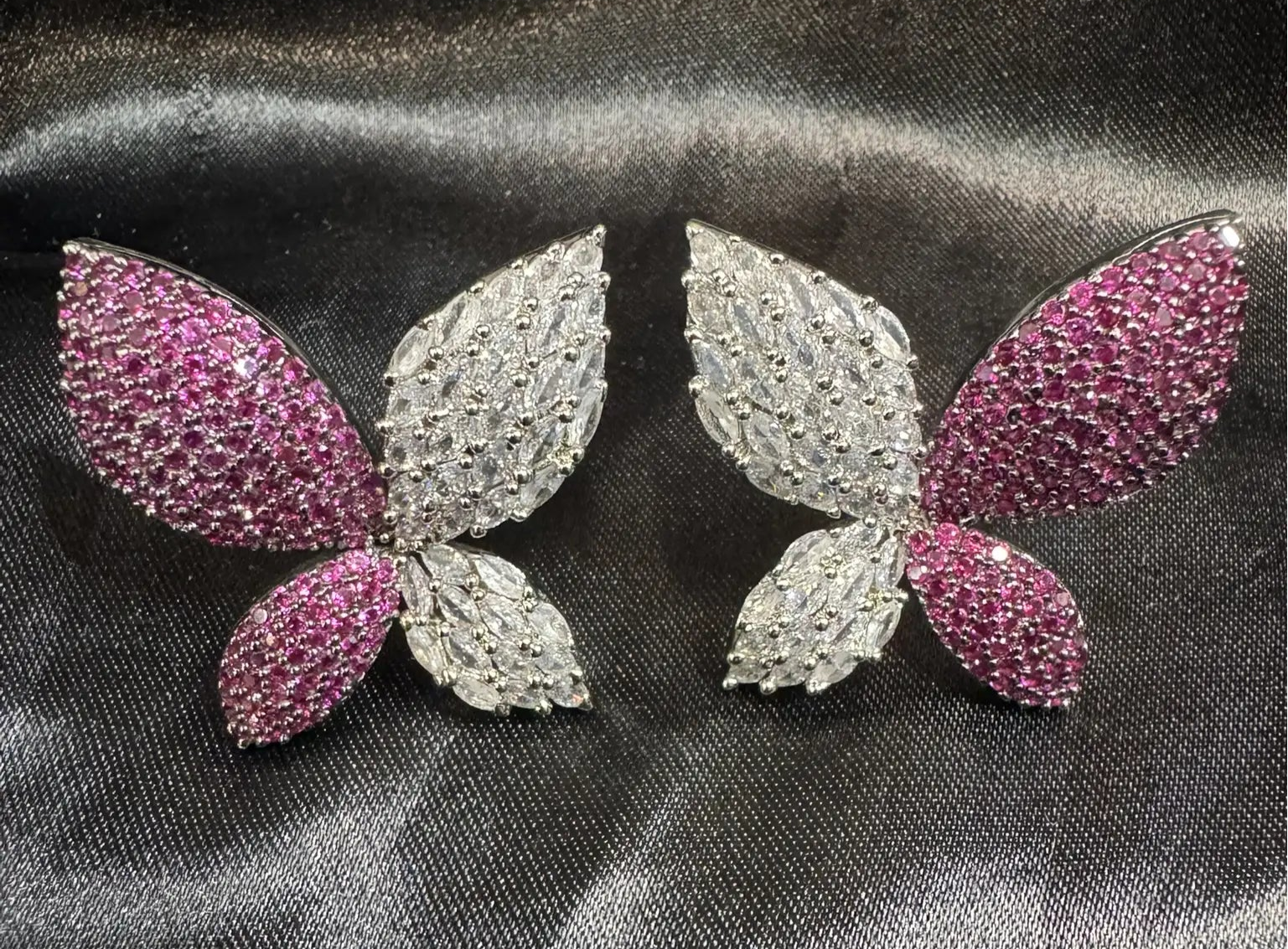 Butterfly-shaped earrings with pink and silver details on a dark fabric background