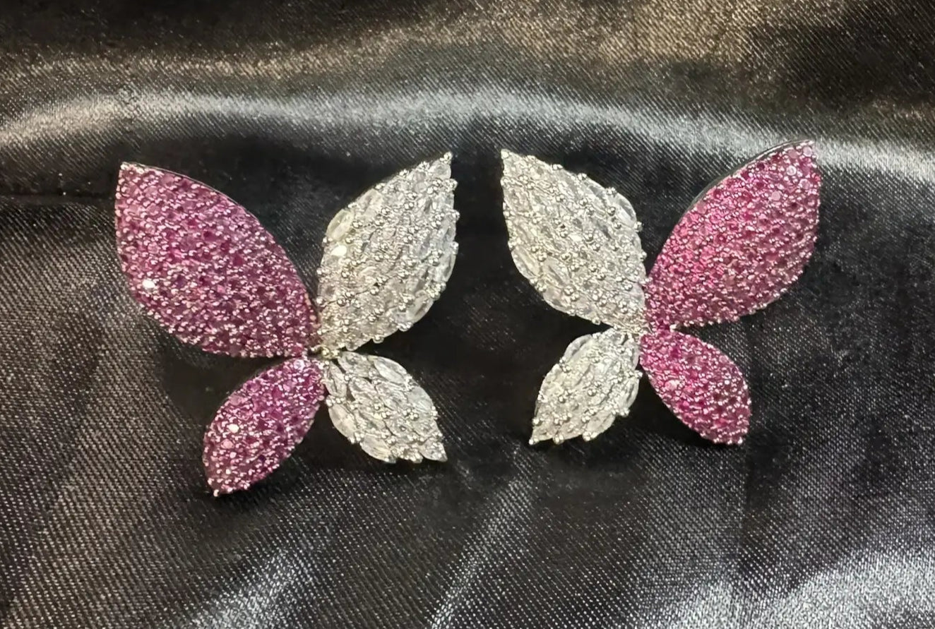 Butterfly-shaped earrings with pink and silver details on a dark fabric background
