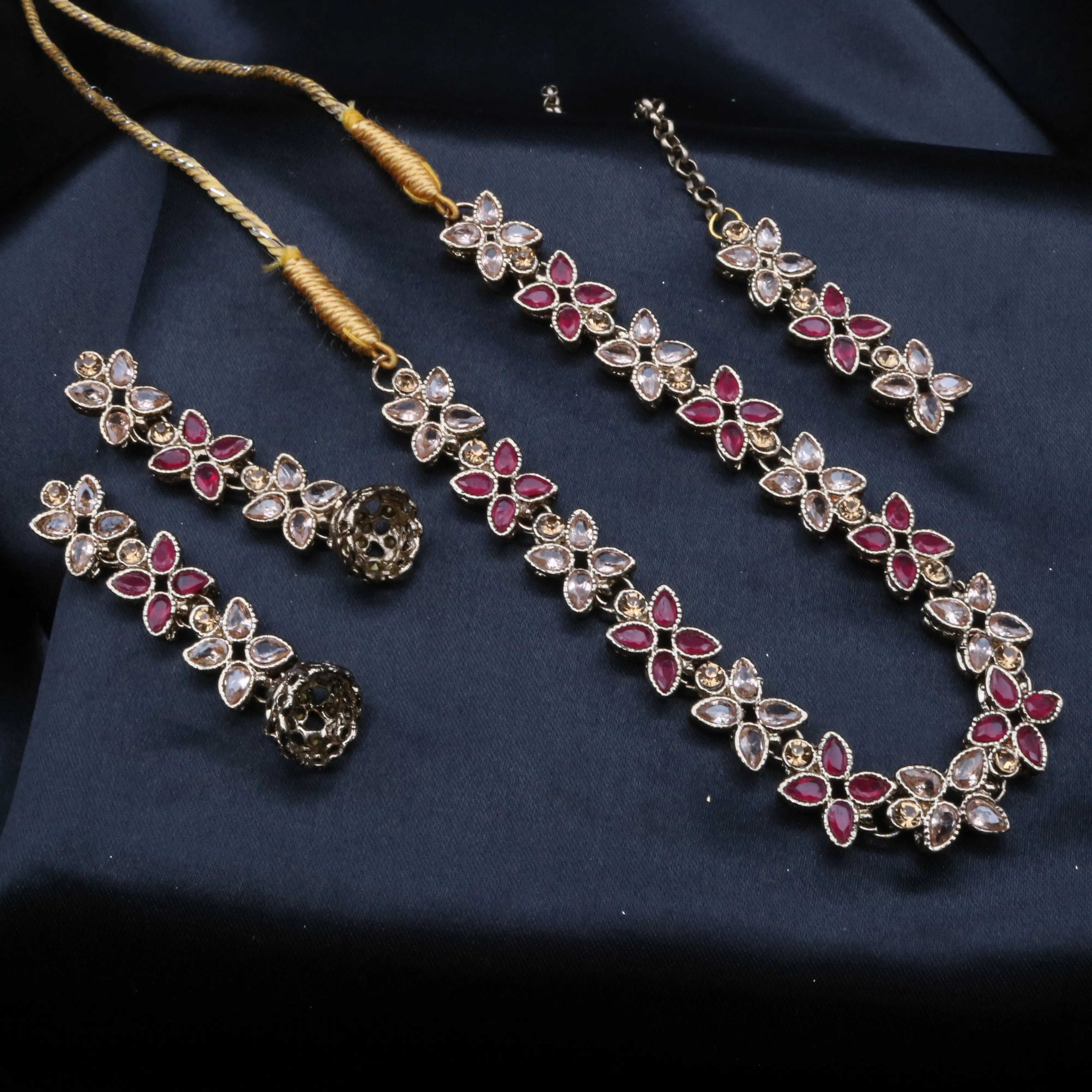 Flora necklace set in red and champagne CZ stones arranged in floral clusters, laid on dark navy fabric.