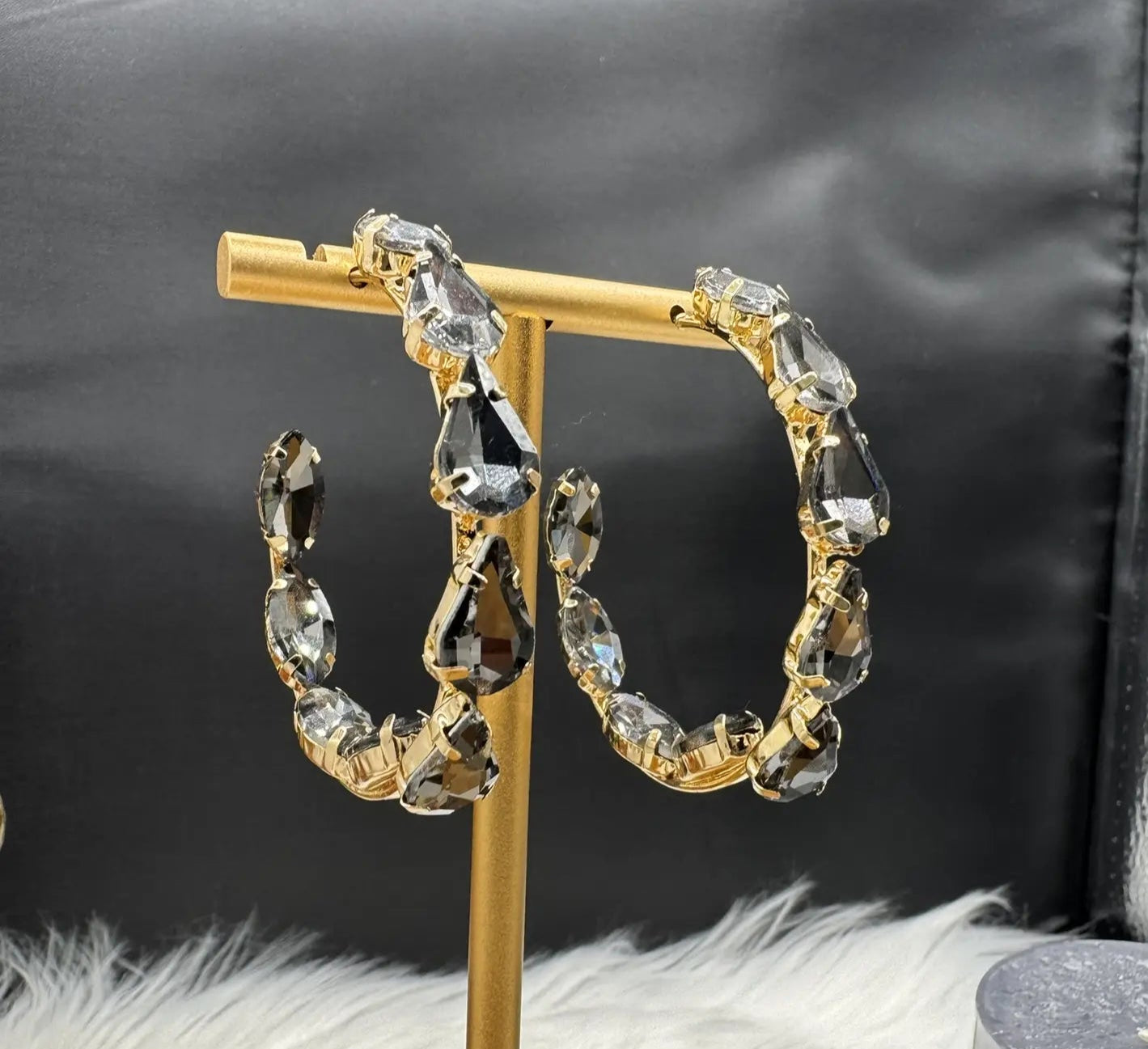 Gold hoop earrings with grey gemstones on a gold stand against a black background